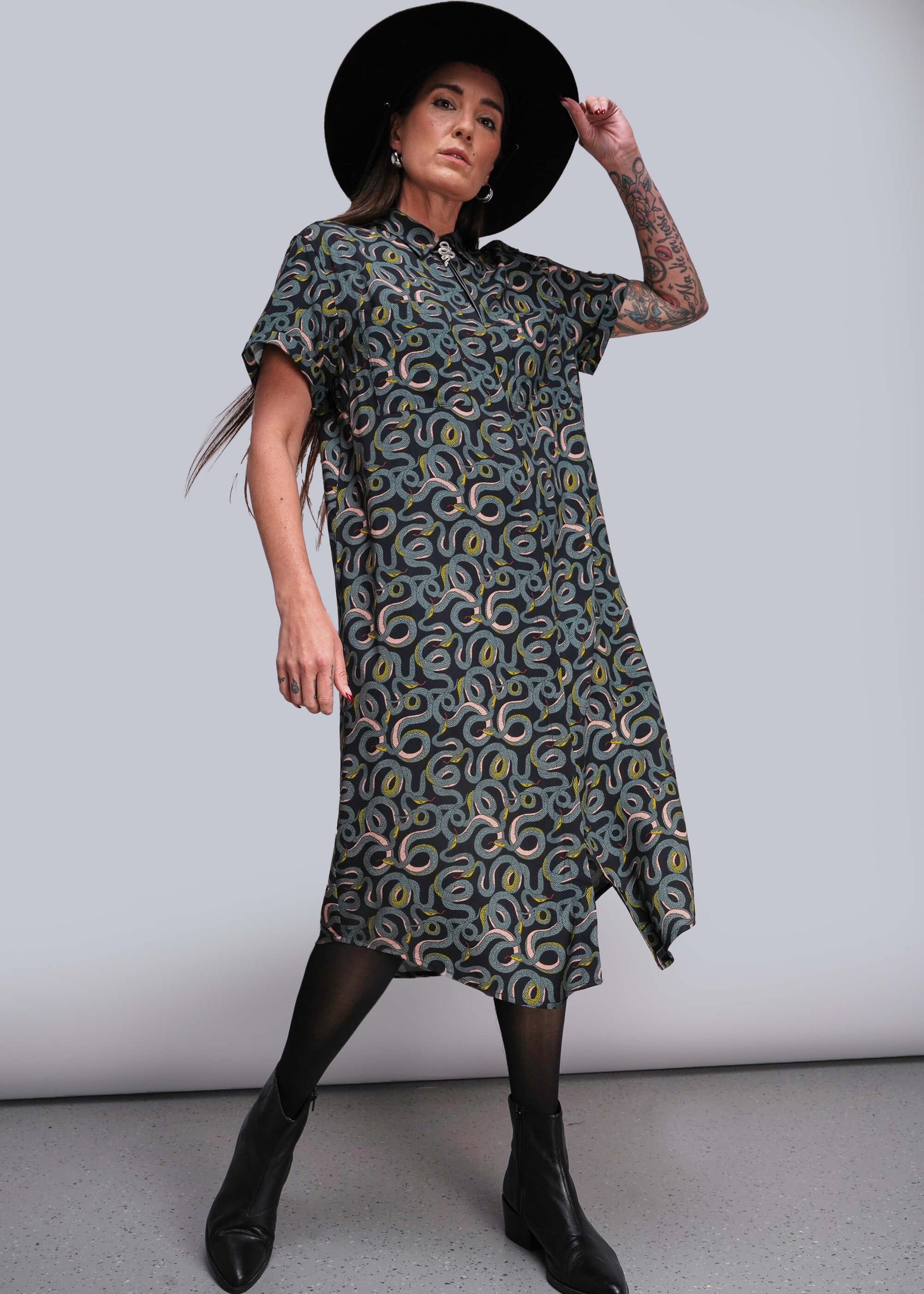S=Woman wearing a patterned dress and black hat against a plain background