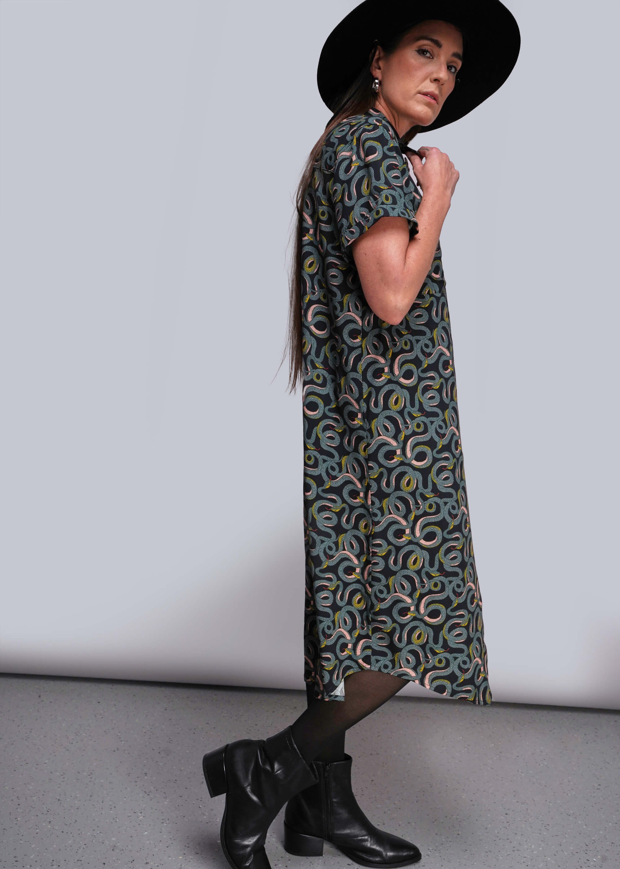 Woman wearing a patterned dress and black hat against a plain background
