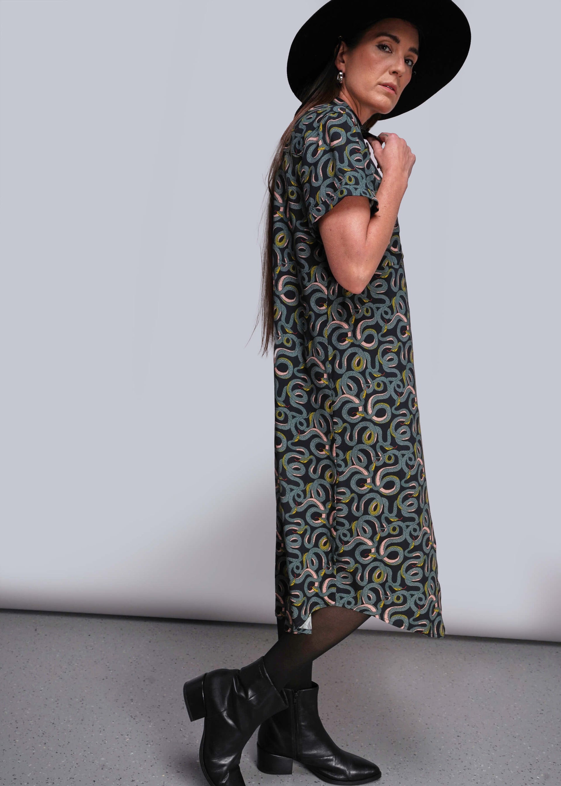 S=Woman wearing a patterned dress and black hat against a plain background
