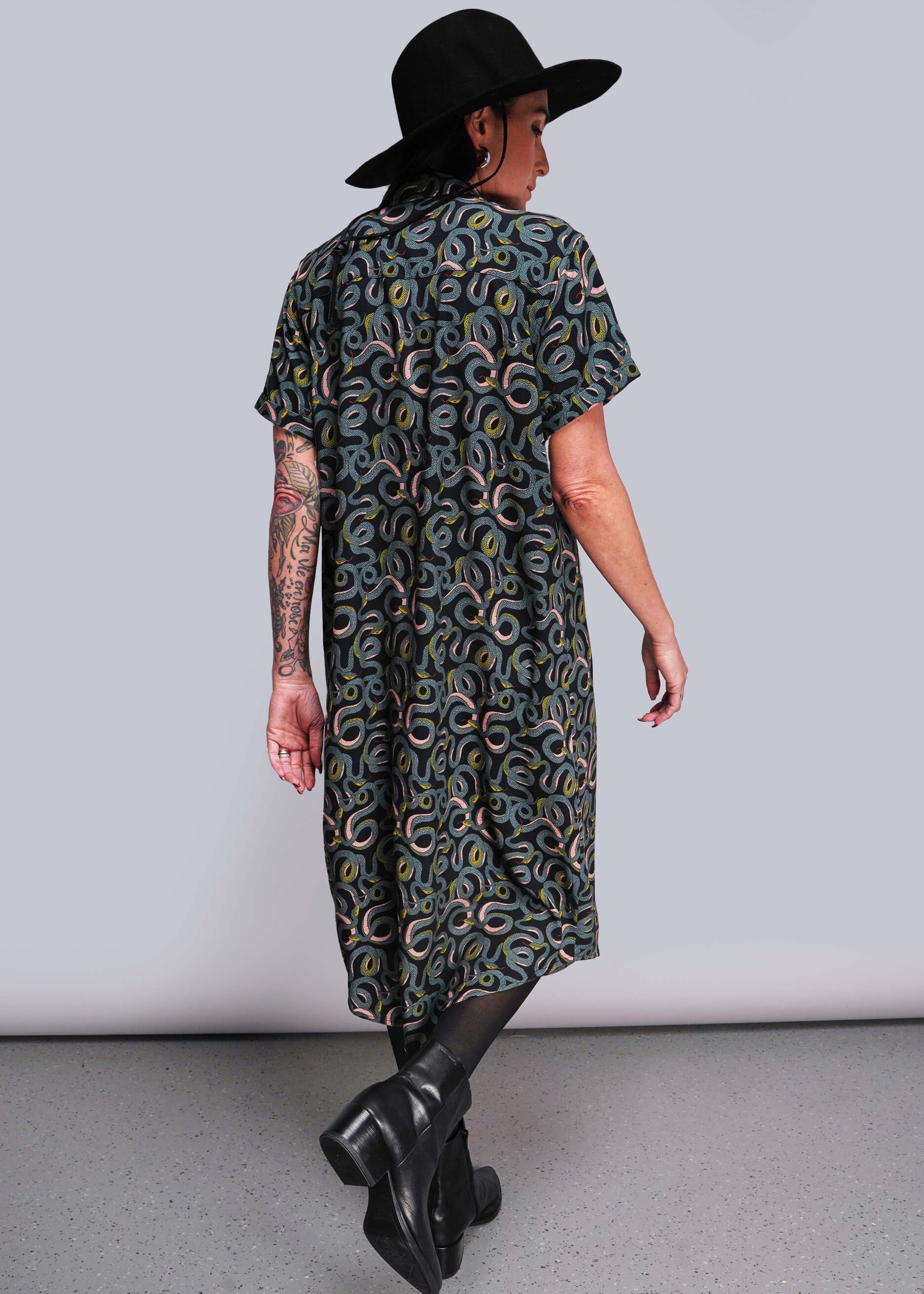 S=Person wearing a patterned dress and black hat against a plain background