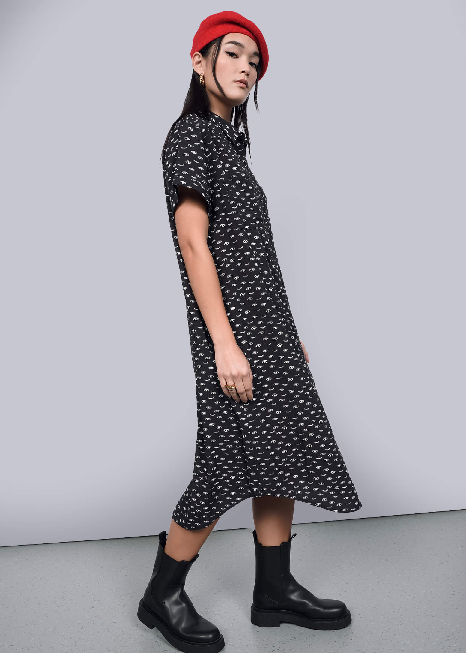 S=A person wearing a red beret, The Empower Shirt Dress in black with a subtle white pattern, and black boots poses confidently against a neutral background. The stylish dress features a modern button closure, completing the chic look.