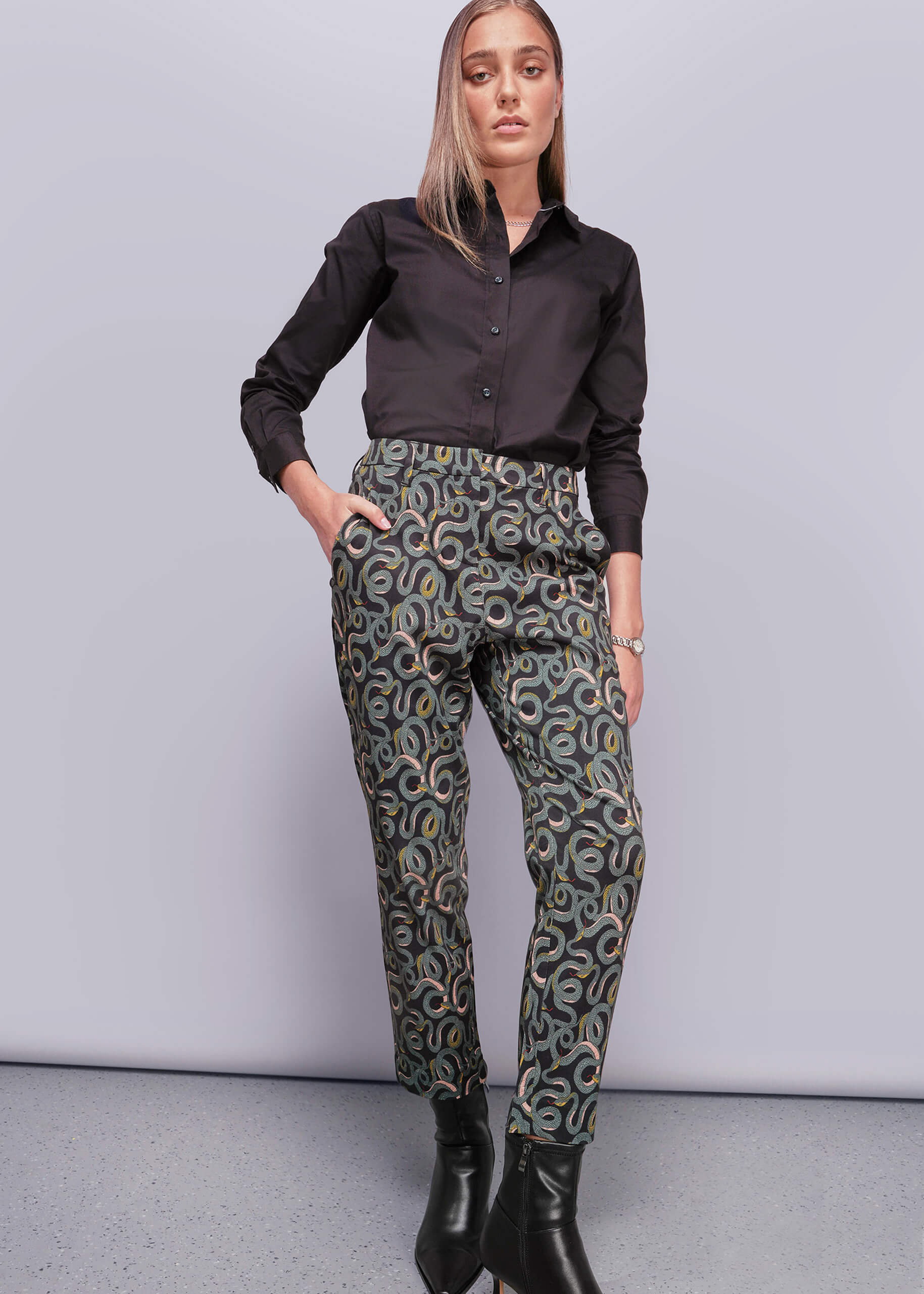 Woman wearing a black shirt and patterned pants against a gray background
