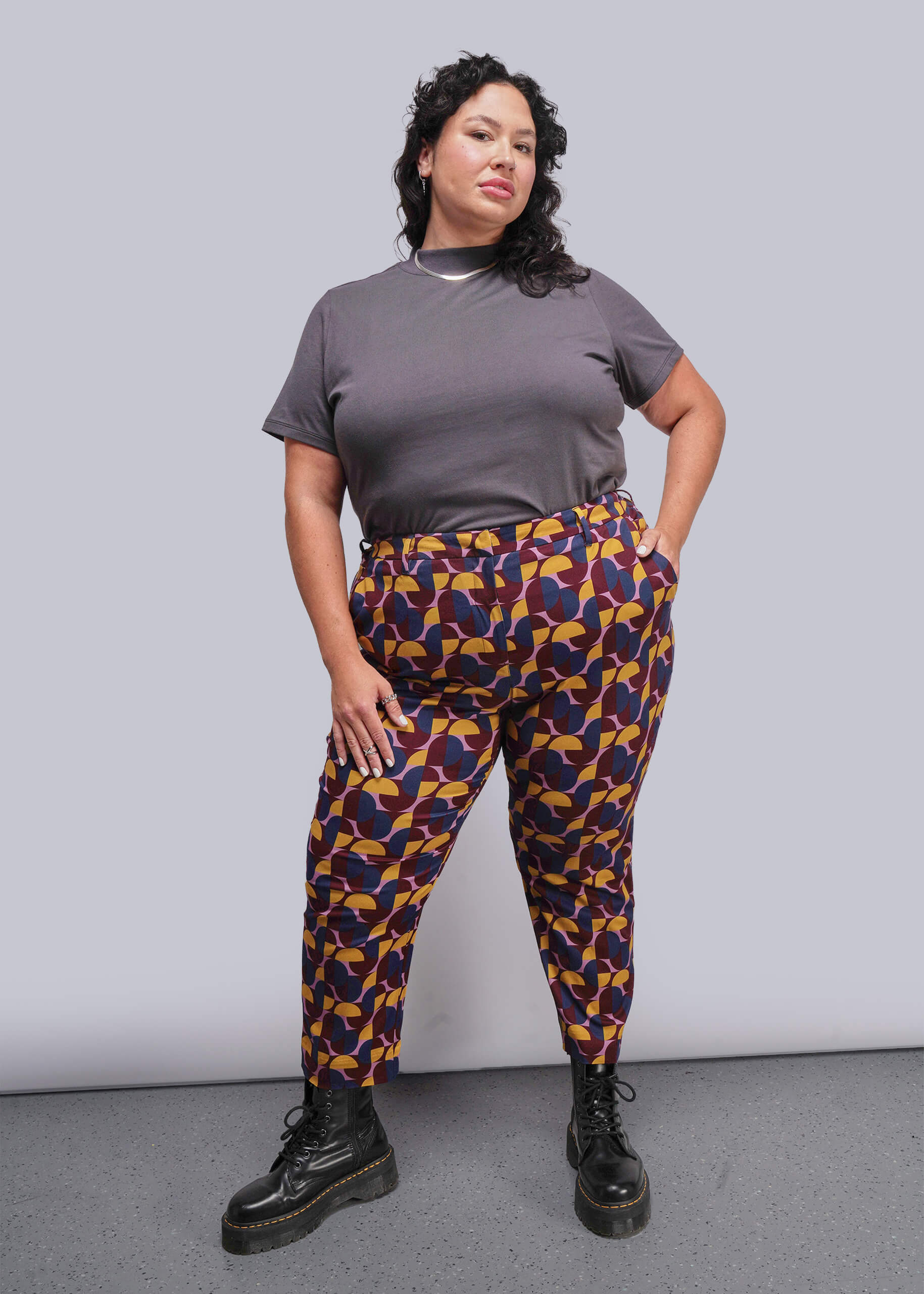 1X=Woman wearing a gray t-shirt and colorful patterned pants against a plain background