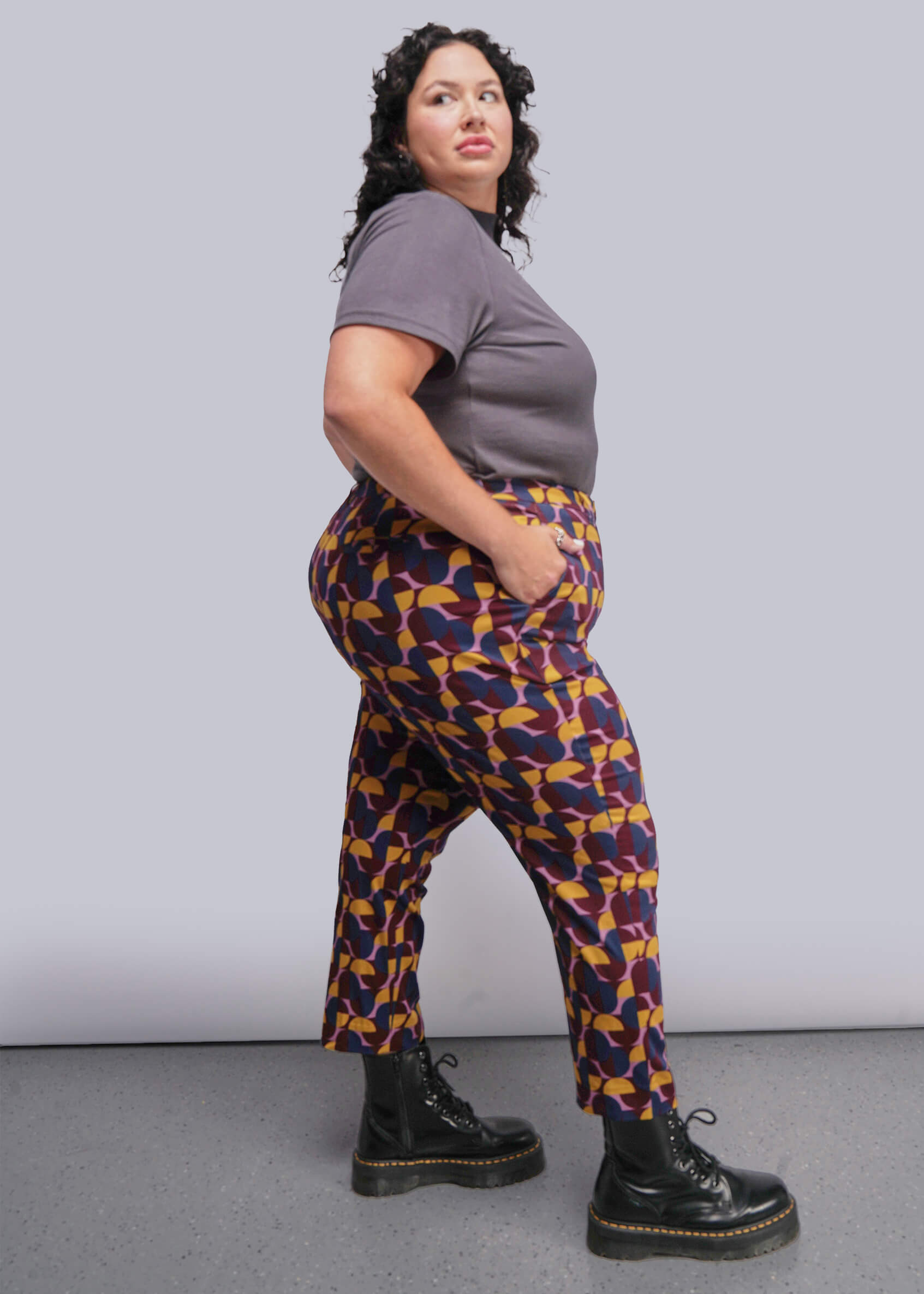 1X=Person wearing a gray shirt and patterned pants against a plain background
