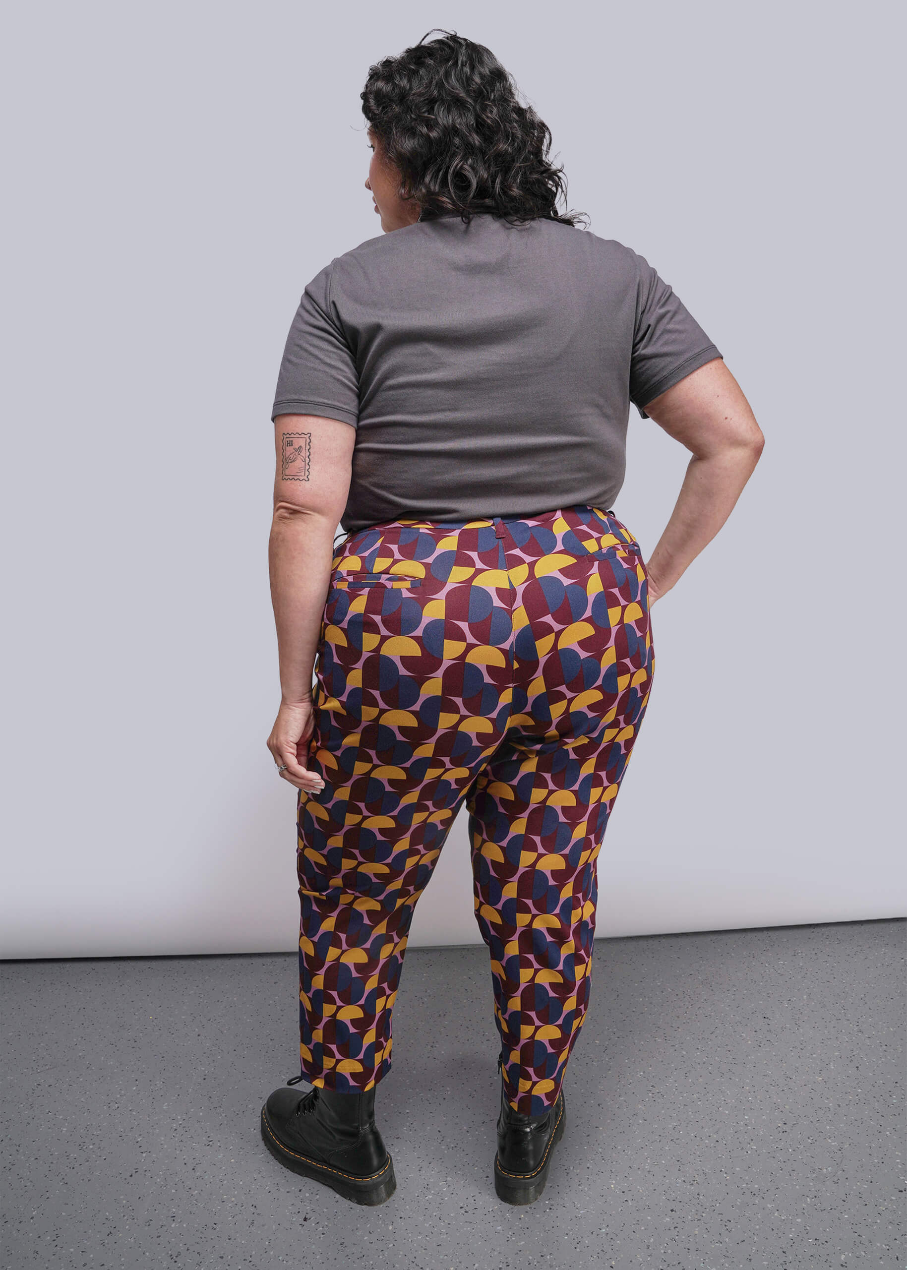1X=Person wearing colorful patterned pants and a gray shirt against a plain background