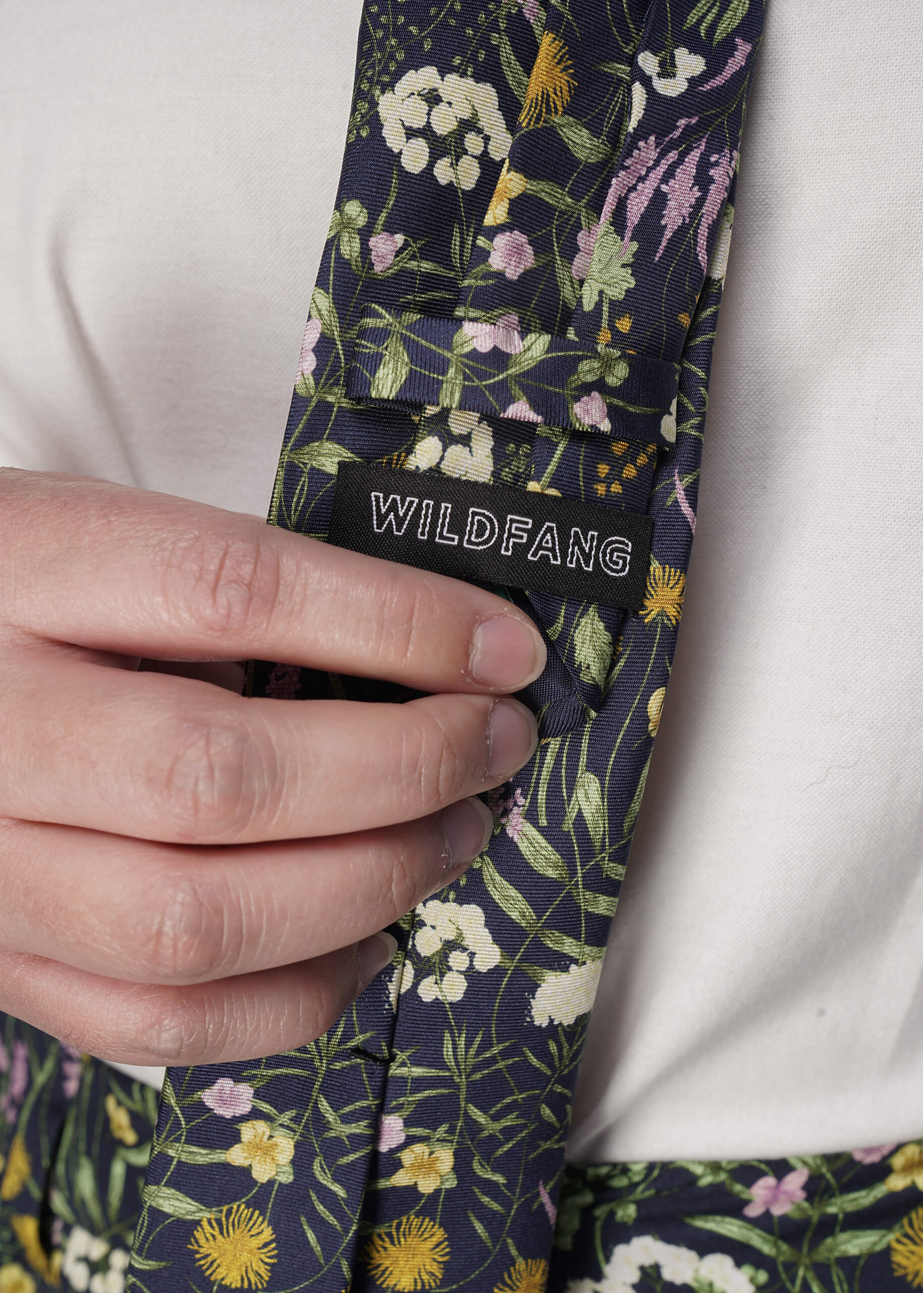 Floral-patterned tie with 'Wildfang' branding held by a hand against a white background