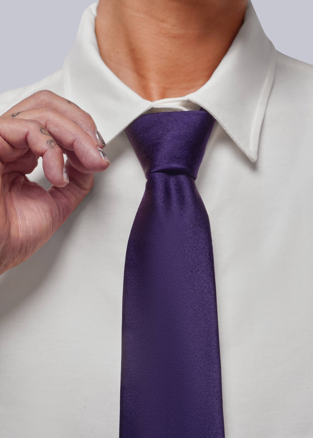 A close-up of a person wearing a white collared dress shirt and a deep purple necktie, with one hand adjusting the collar.