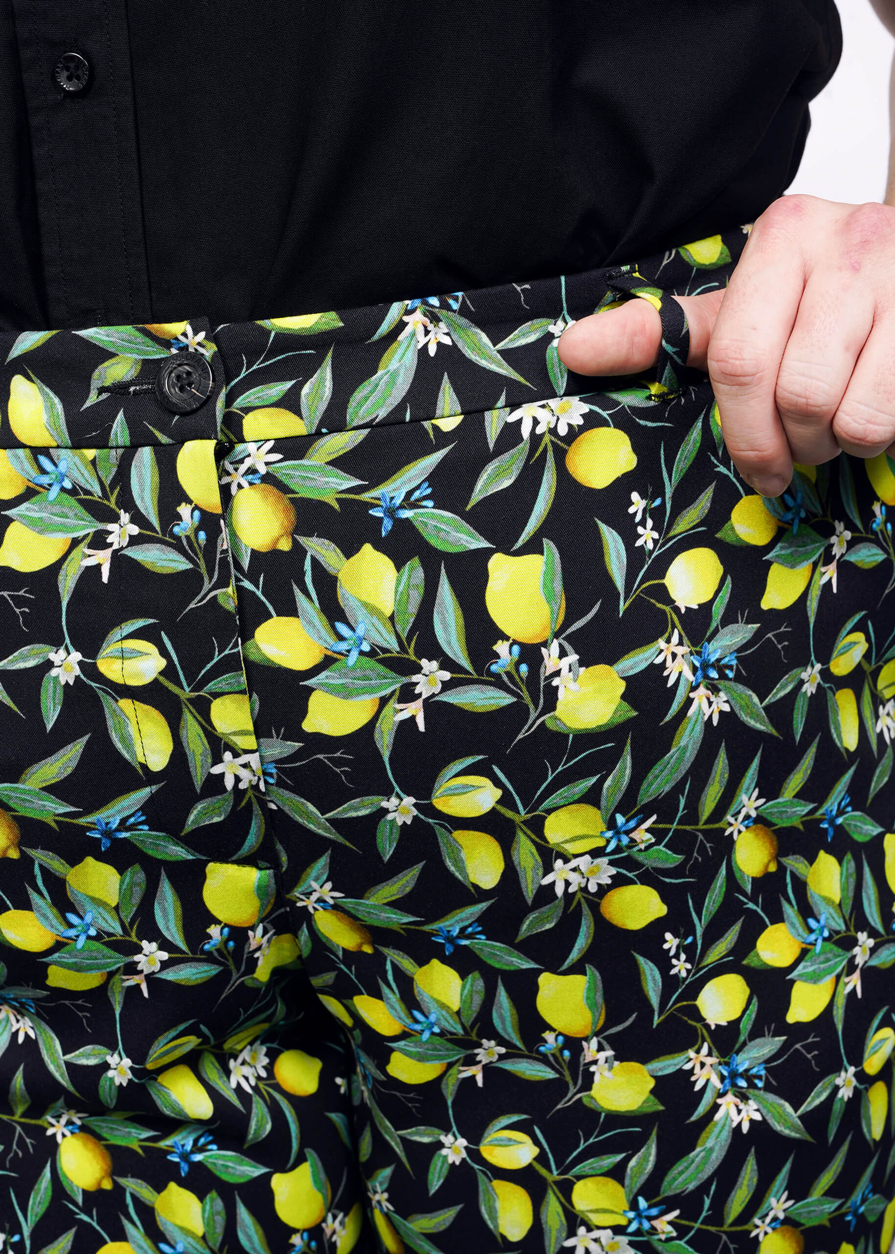 1X=Close up view of model with hand in front pant belt loop of The Empower Trouser in Citrus Black, which is a yellow and green print on black background featuring lemons and leaves. 
