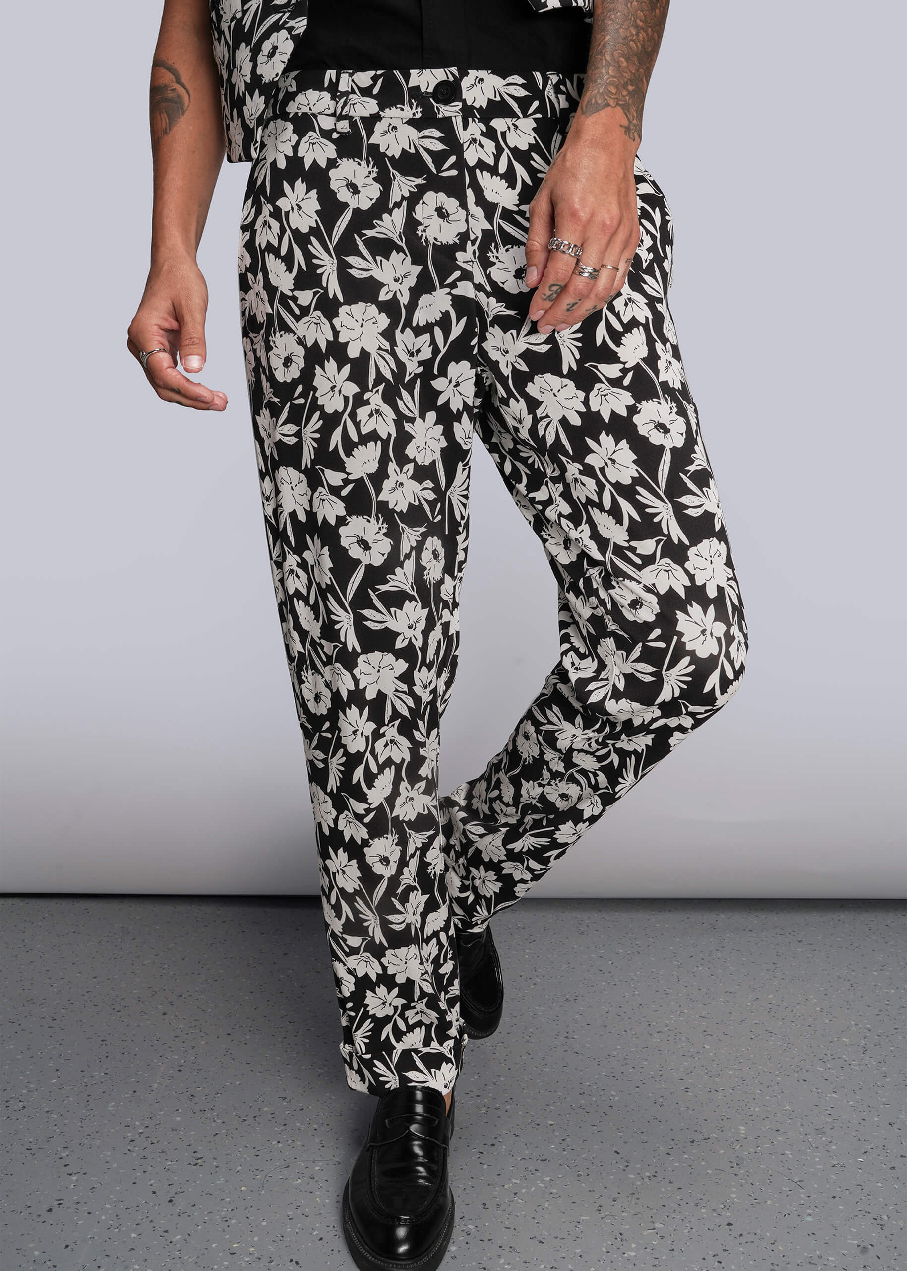 Pictured from waist down, person wearing black and white floral pants against a plain background