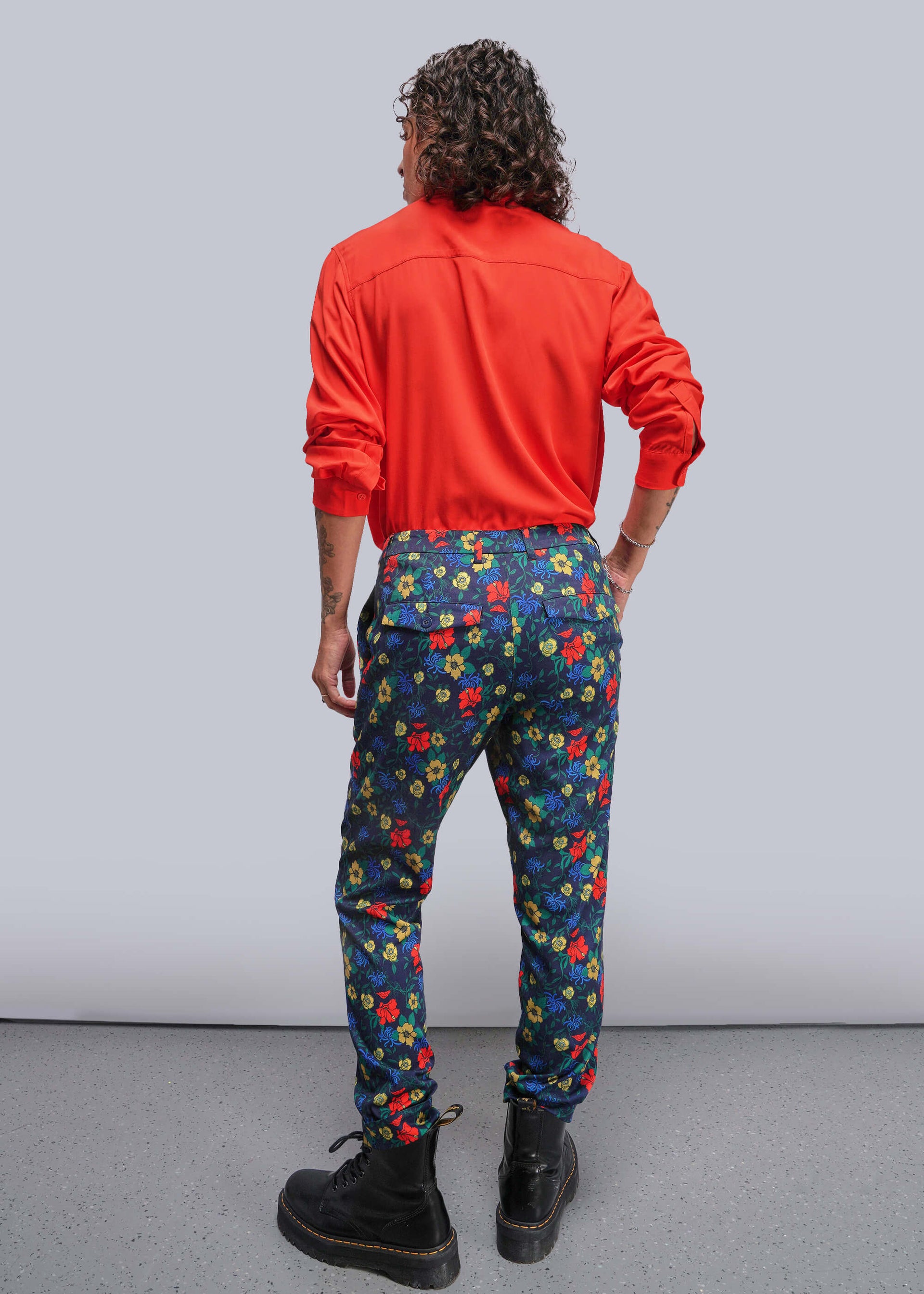 S=Person wearing a red jacket and colorful floral pants against a gray background