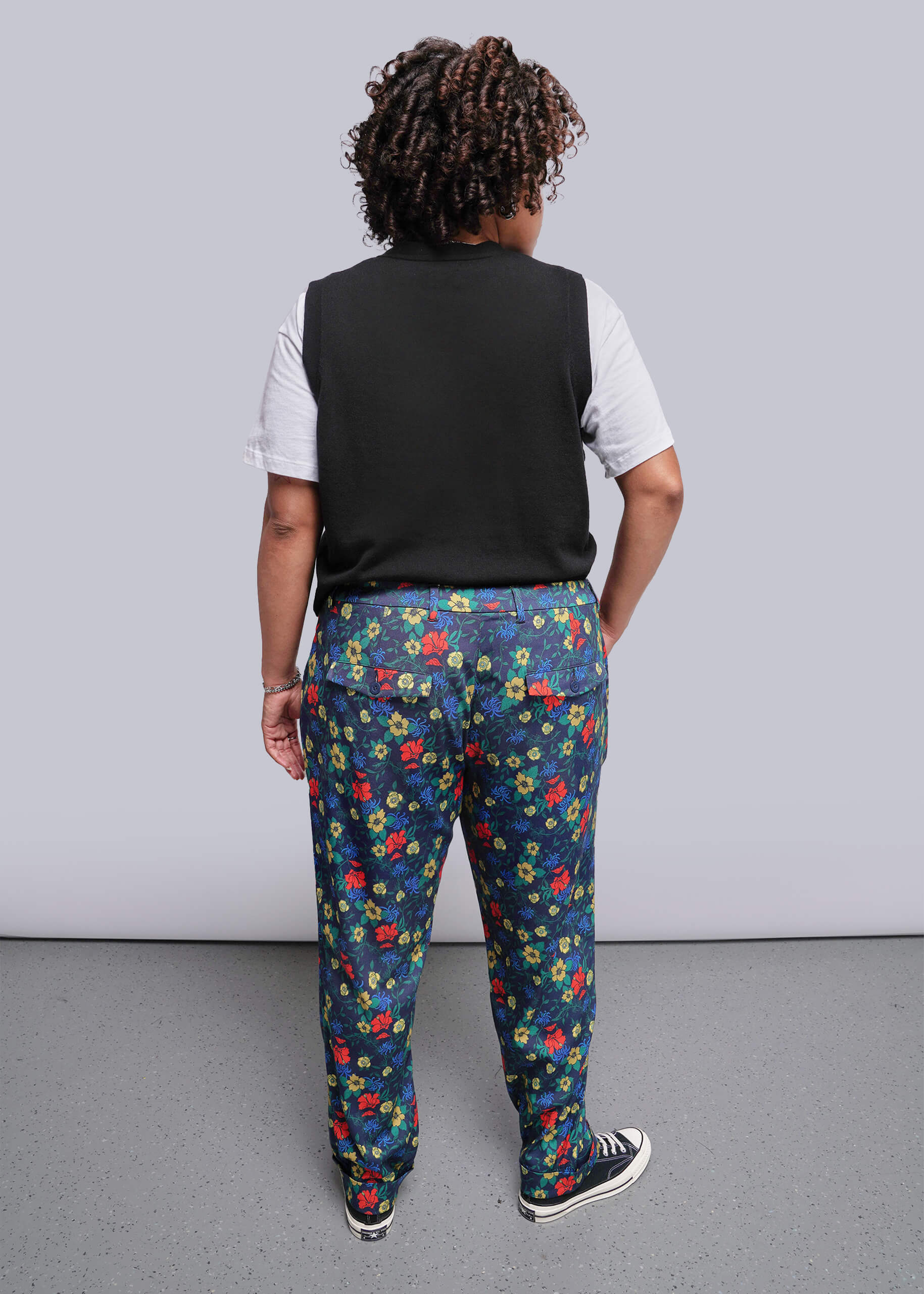 1X=Person wearing a black vest, white shirt, and colorful floral pants against a plain background