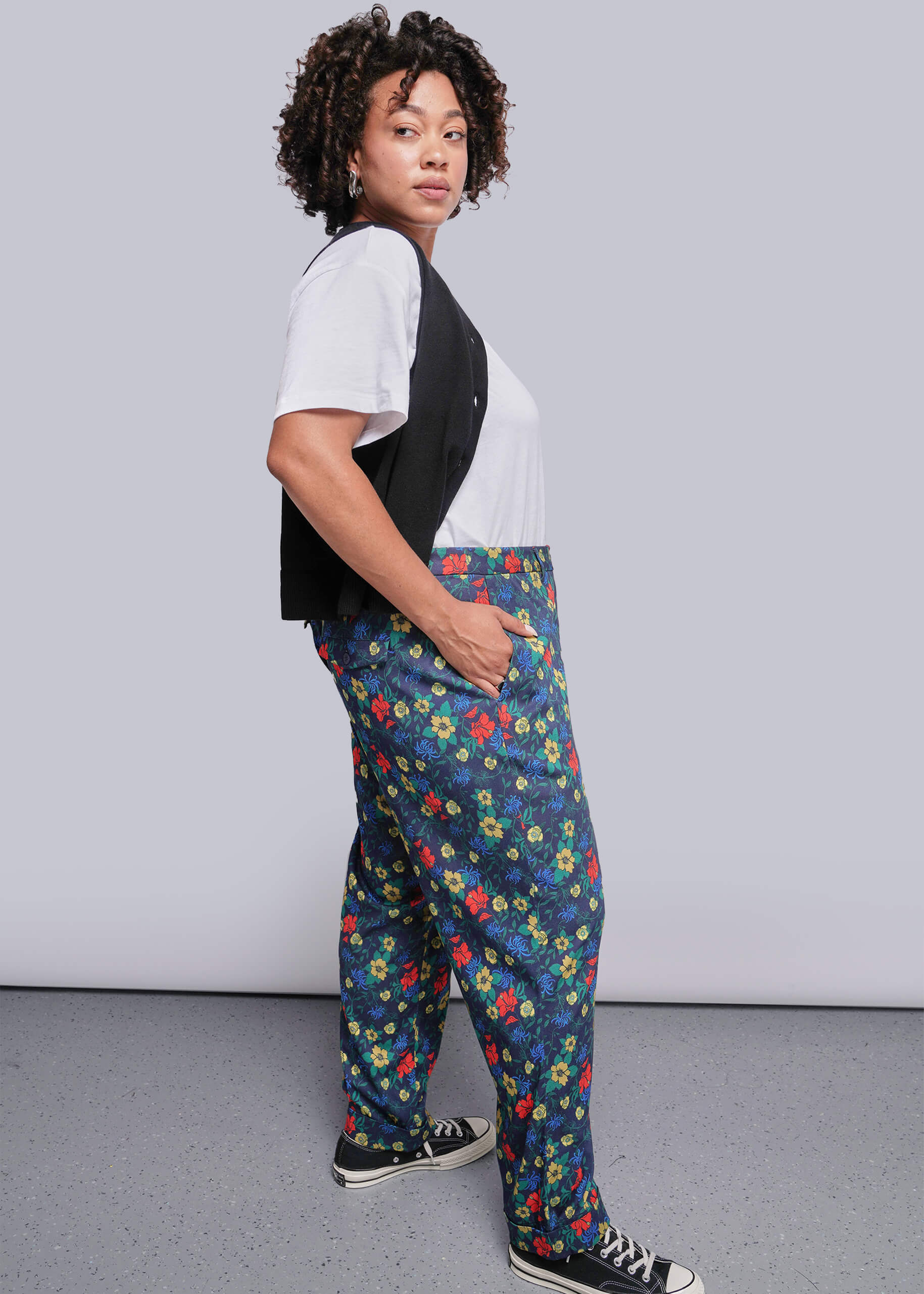1X=Person wearing a white and black top with colorful floral pants against a plain background