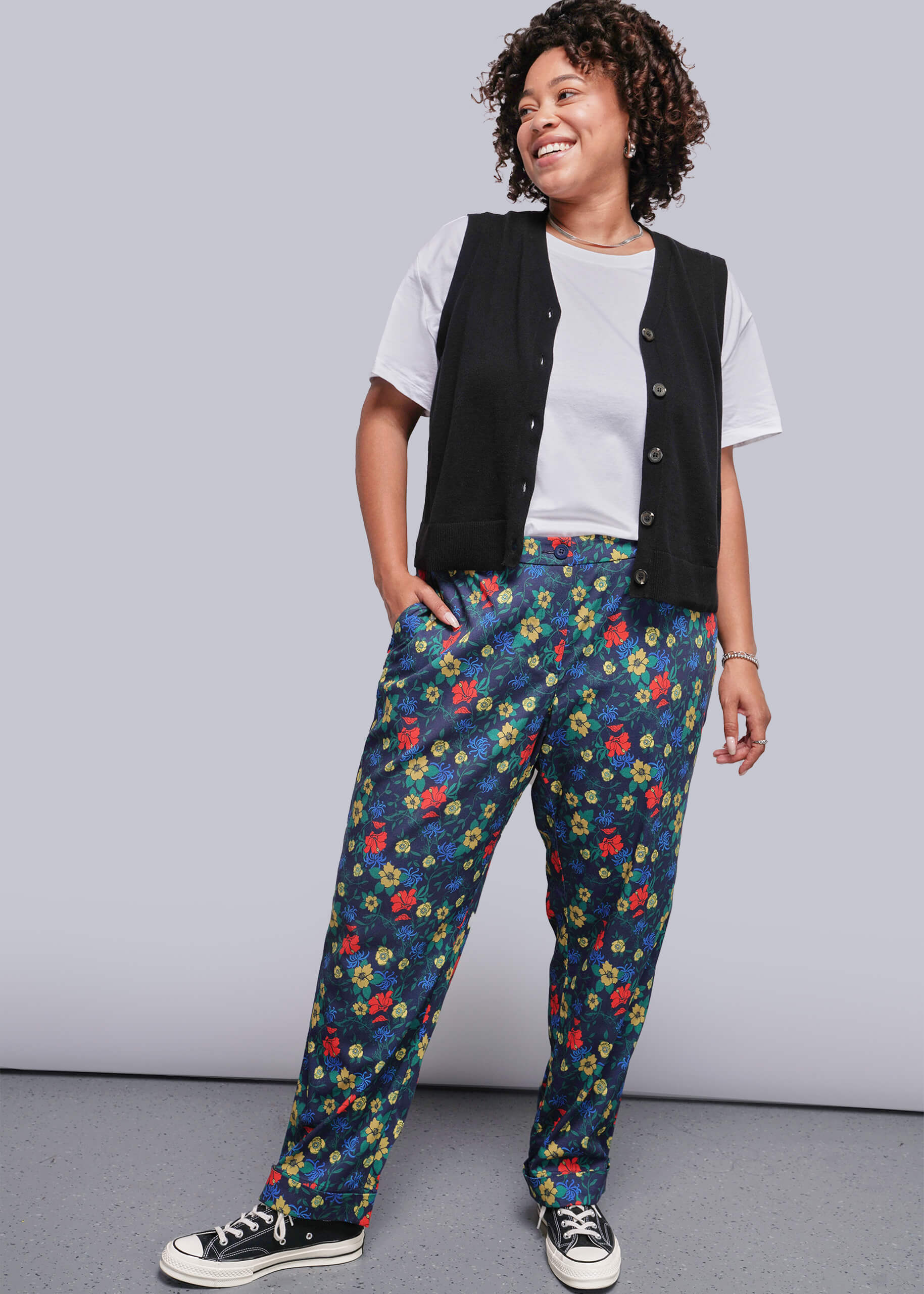 1X=Person wearing a black vest, white shirt, and colorful floral pants against a gray background
