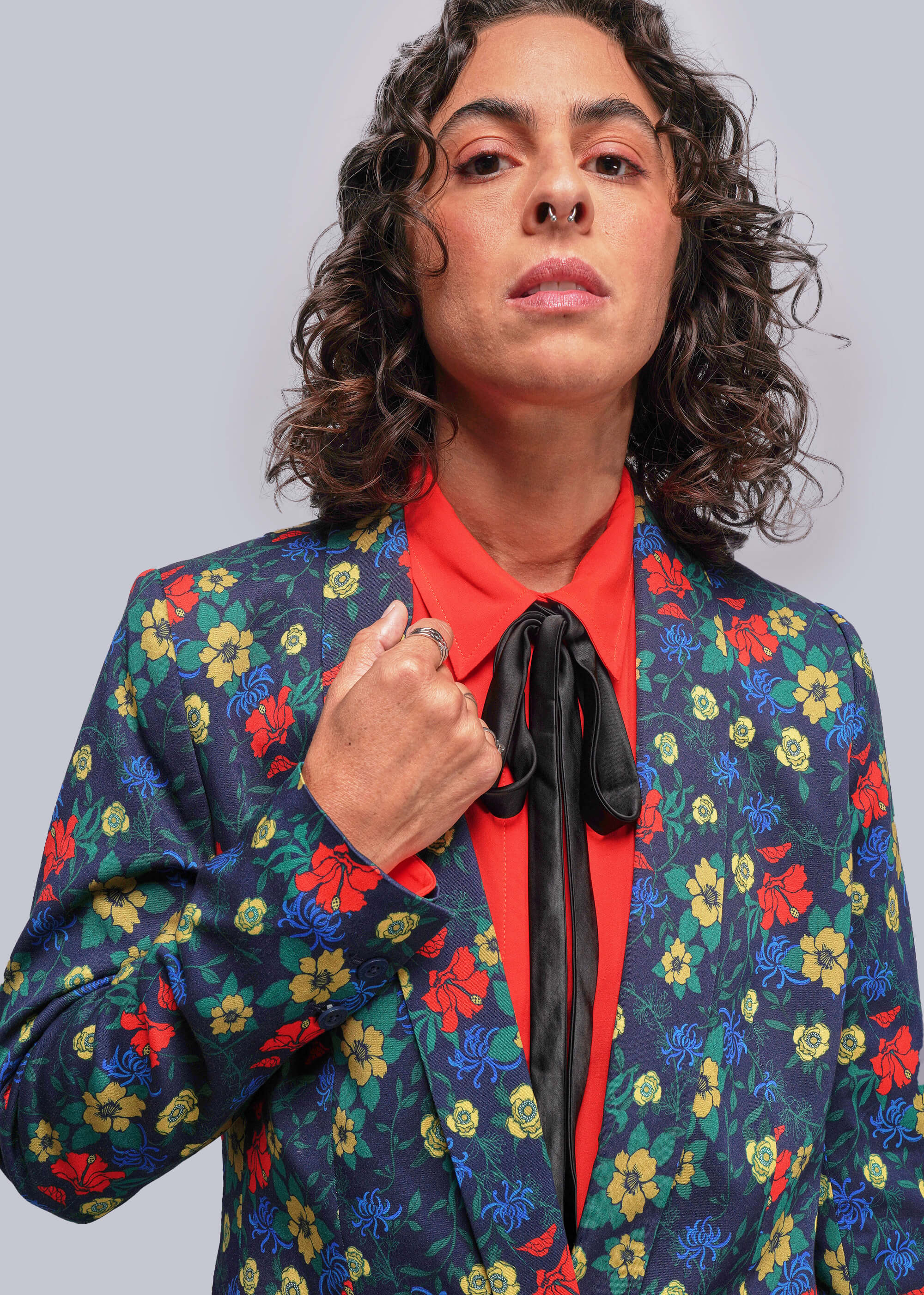 Person wearing a colorful floral blazer over a red shirt with a plain background