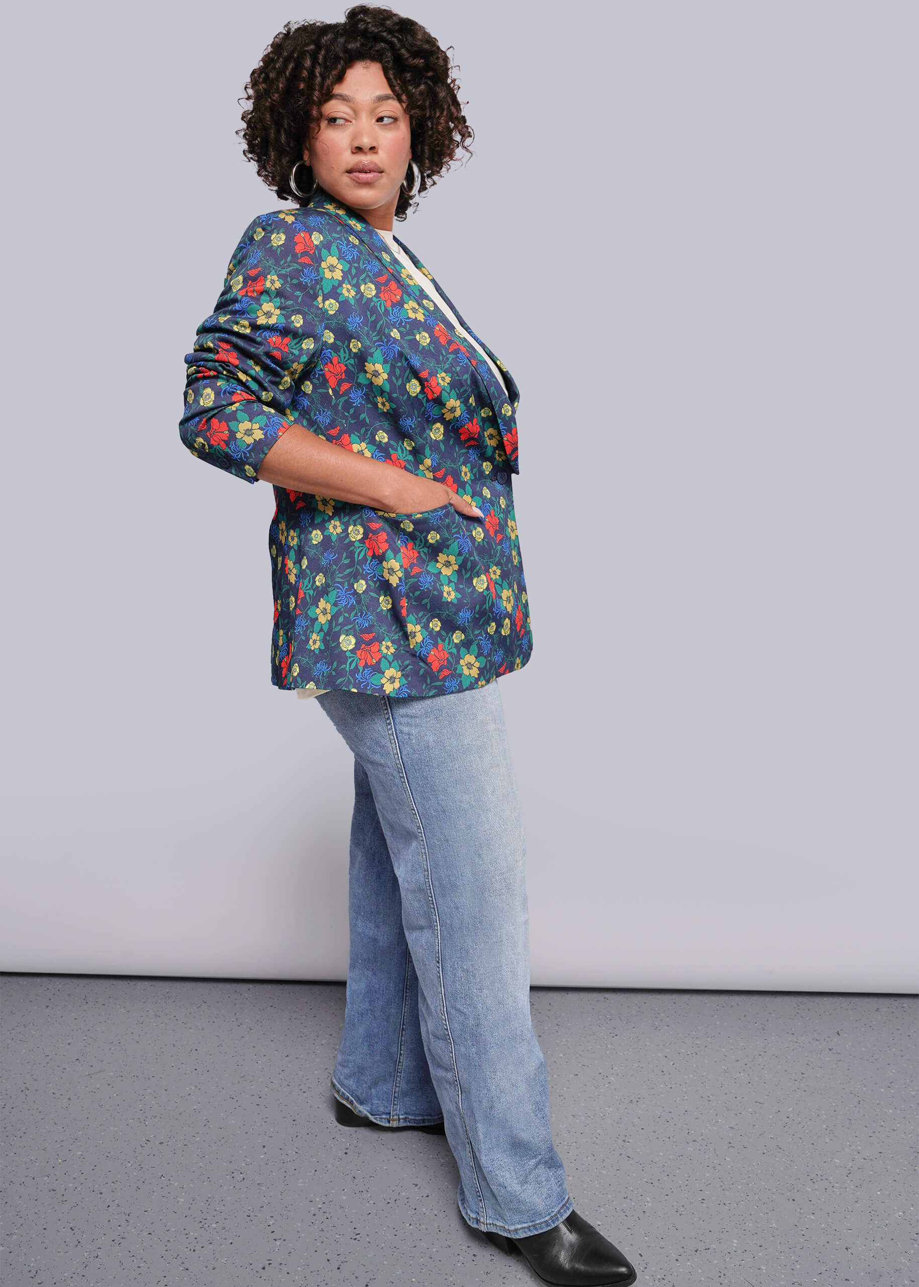 1X=Person wearing a colorful floral blazer and blue jeans against a plain background