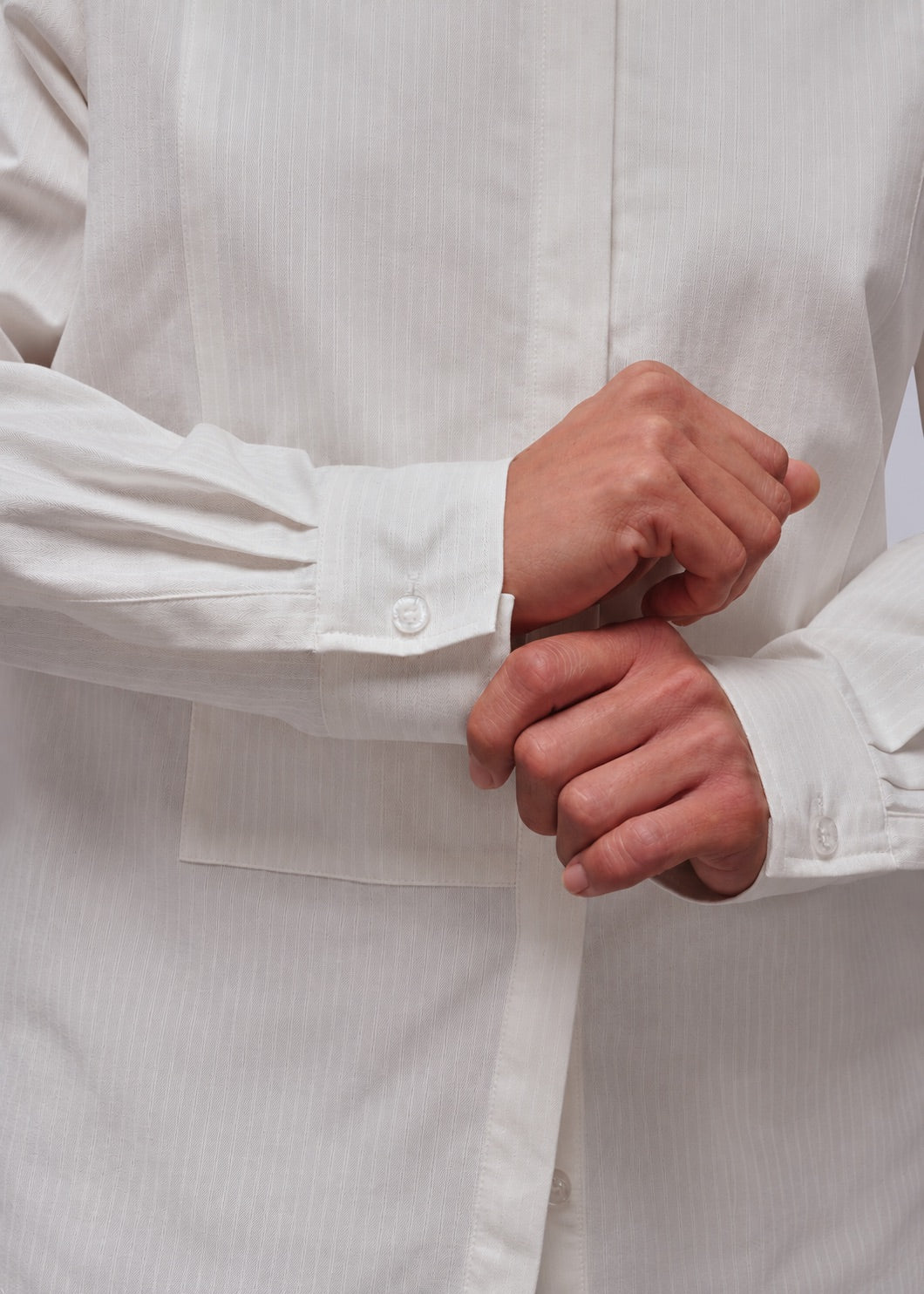 S=Close-up of a person wearing a white long-sleeve button-up shirt, adjusting the cuff with both hands.