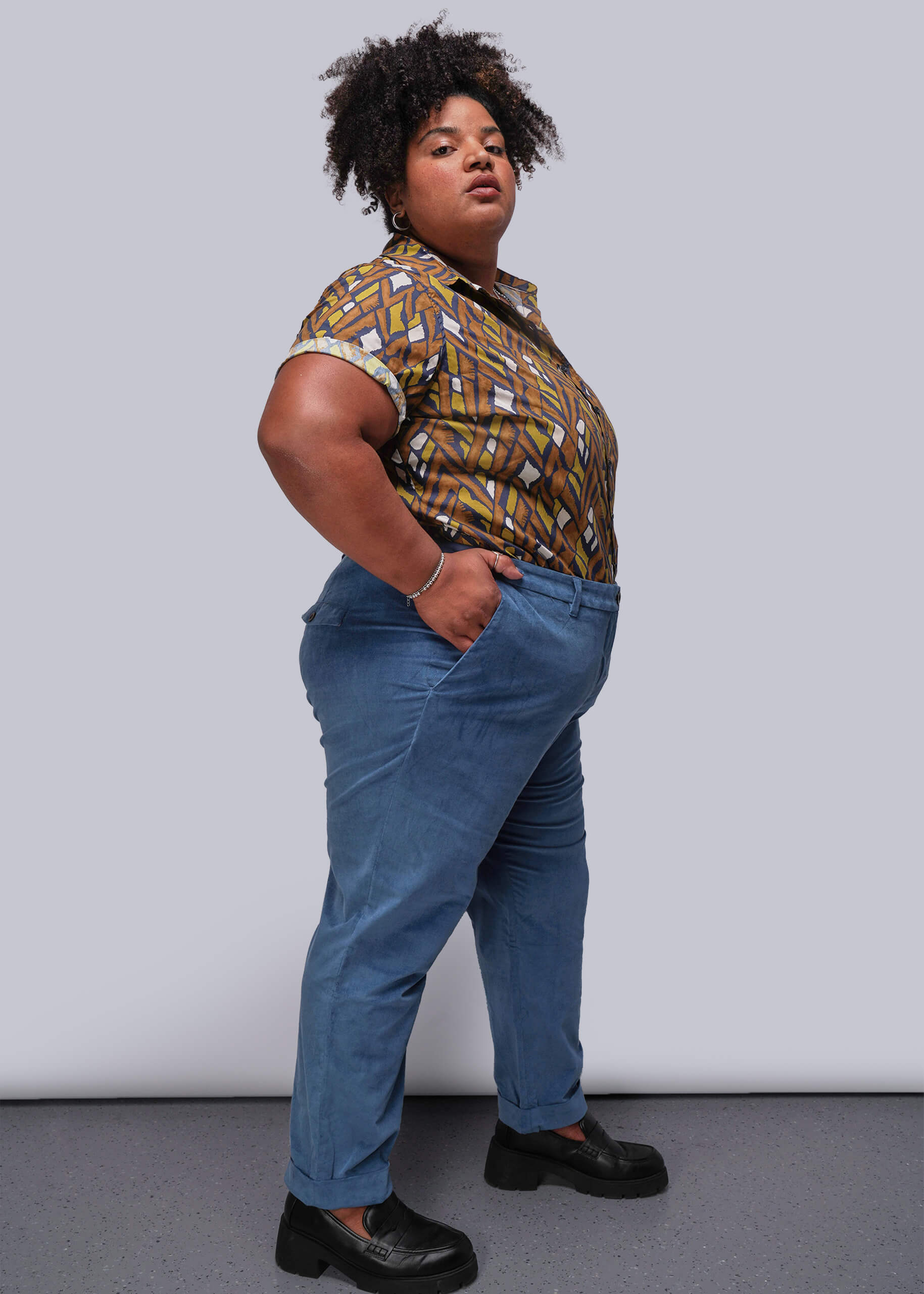 1X=Person wearing a patterned shirt and blue jeans against a plain background