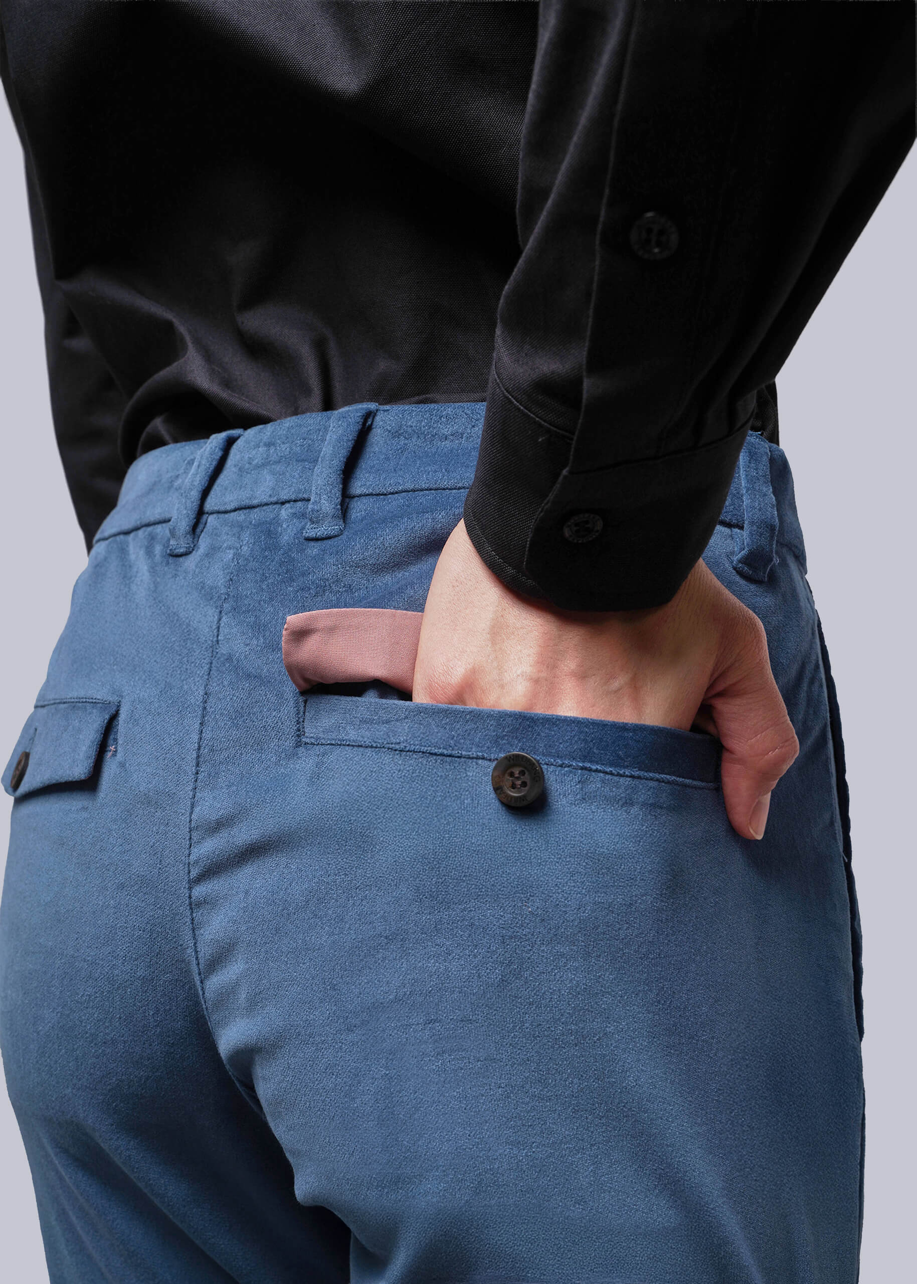 S=Person wearing blue pants and a black shirt with one hand in the pocket against a gray background