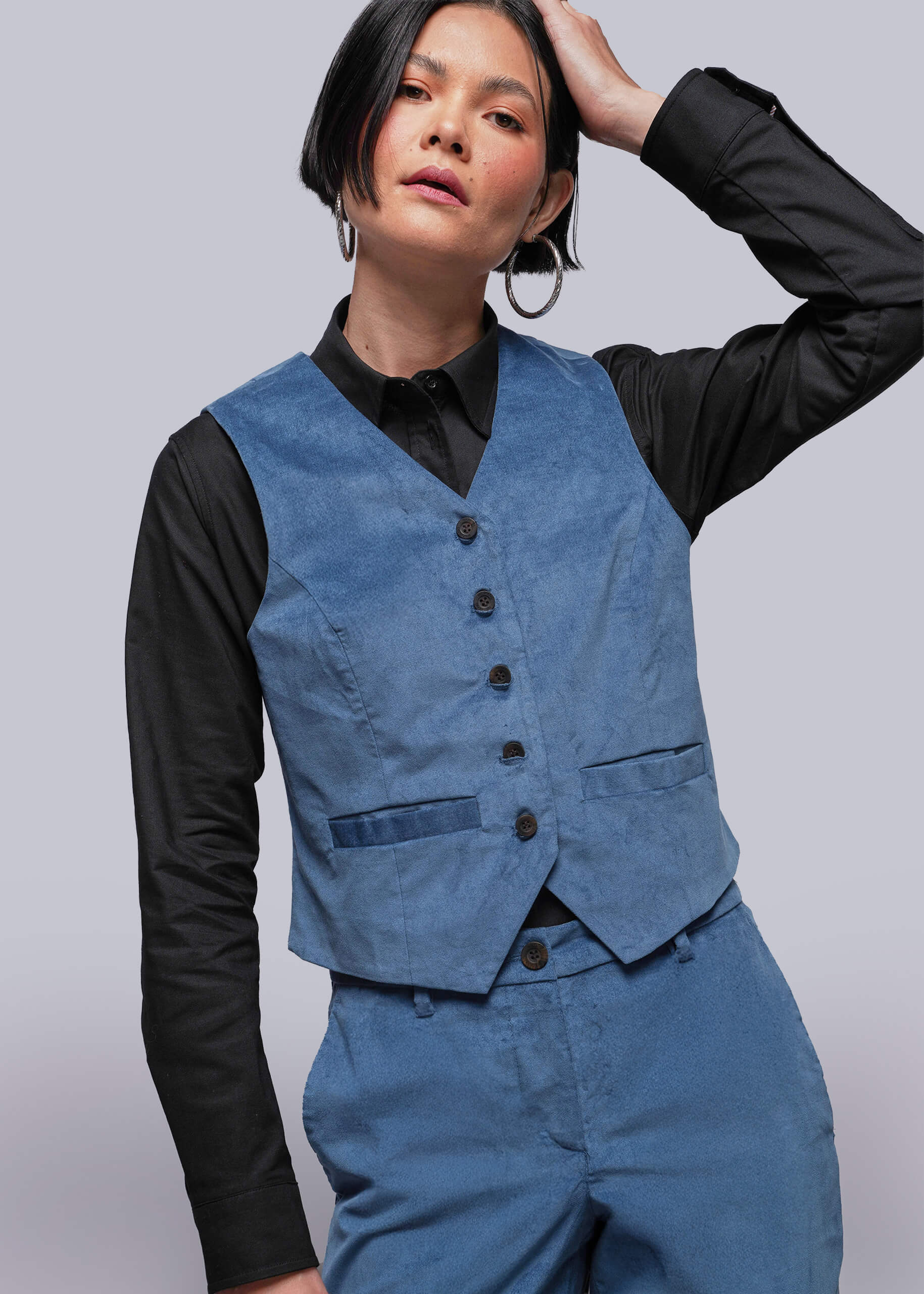Person wearing a blue vest over a black shirt on a plain background