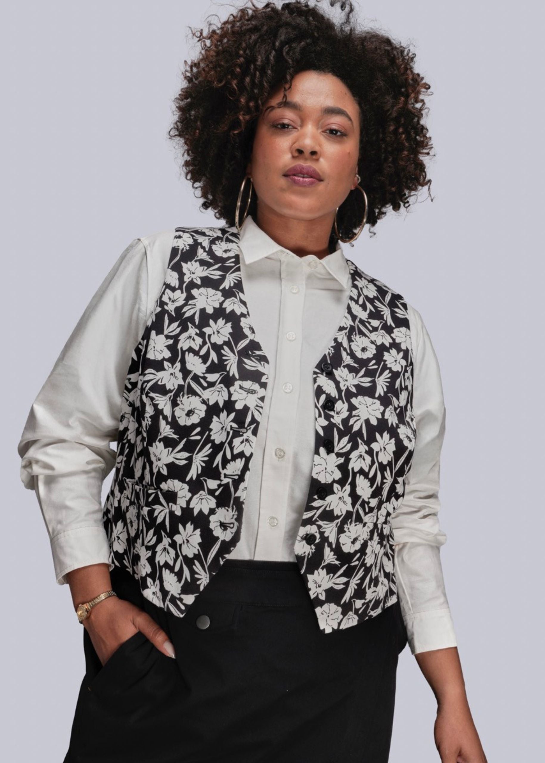1X=Person wearing a black and white floral vest over a white shirt on a light gray background