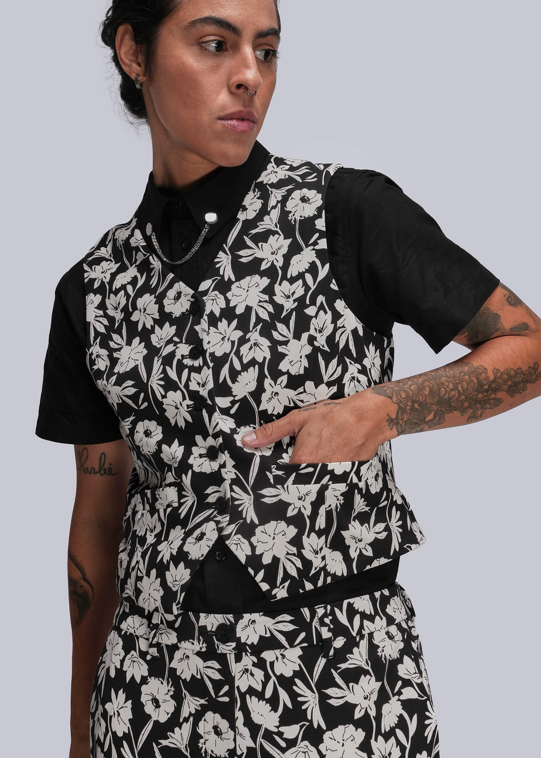 S=Person wearing a black and white floral vest over a black shirt on a light gray background