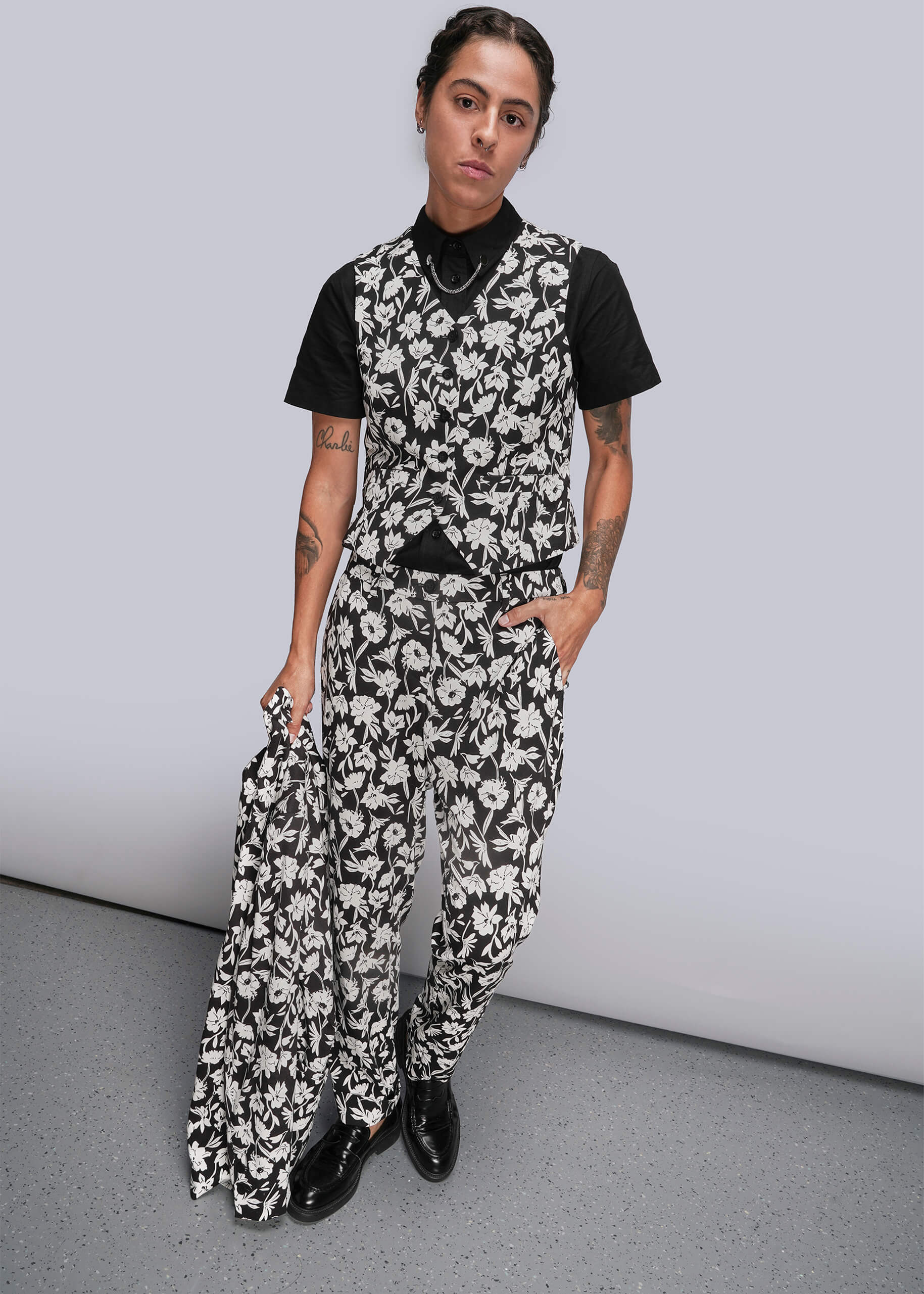 S=Person wearing a black and white floral suit against a gray background