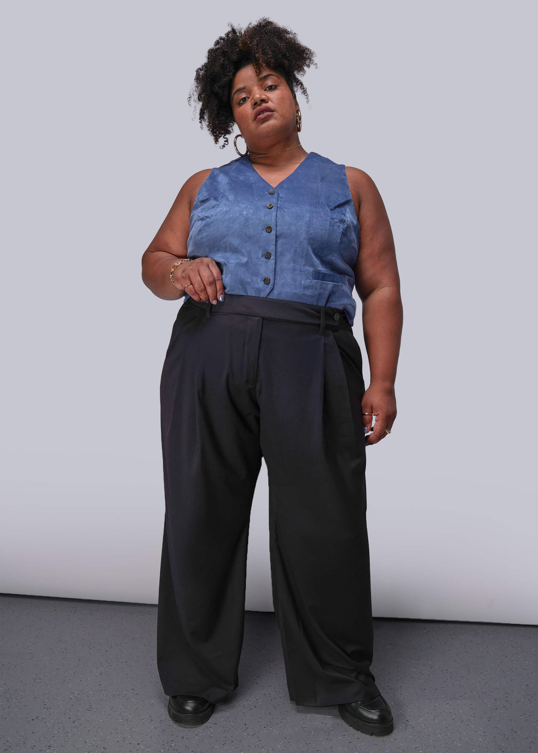 1X=Person wearing a blue sleeveless top and black pants against a plain background