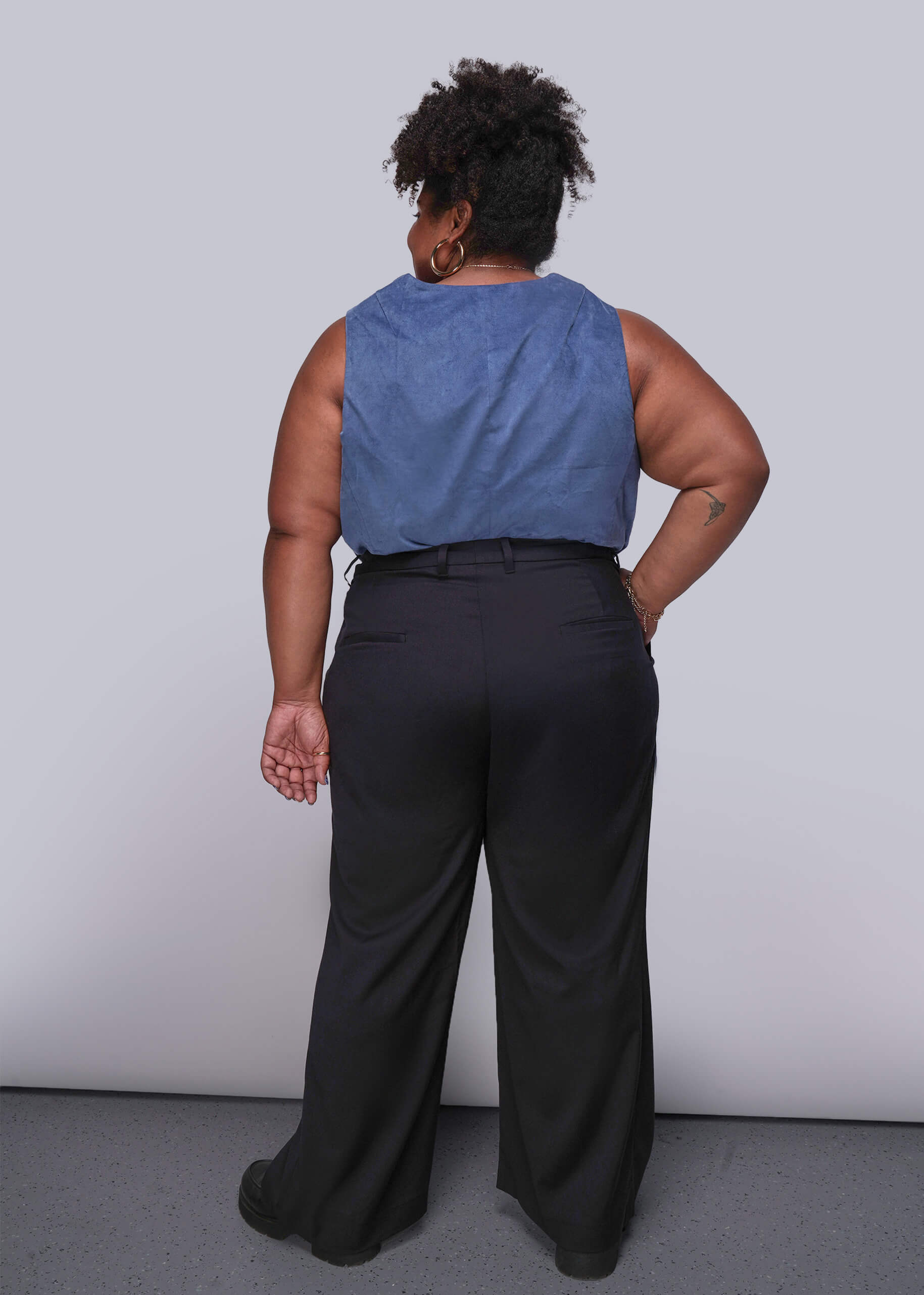 1X=Person wearing a blue sleeveless top and black pants against a plain background