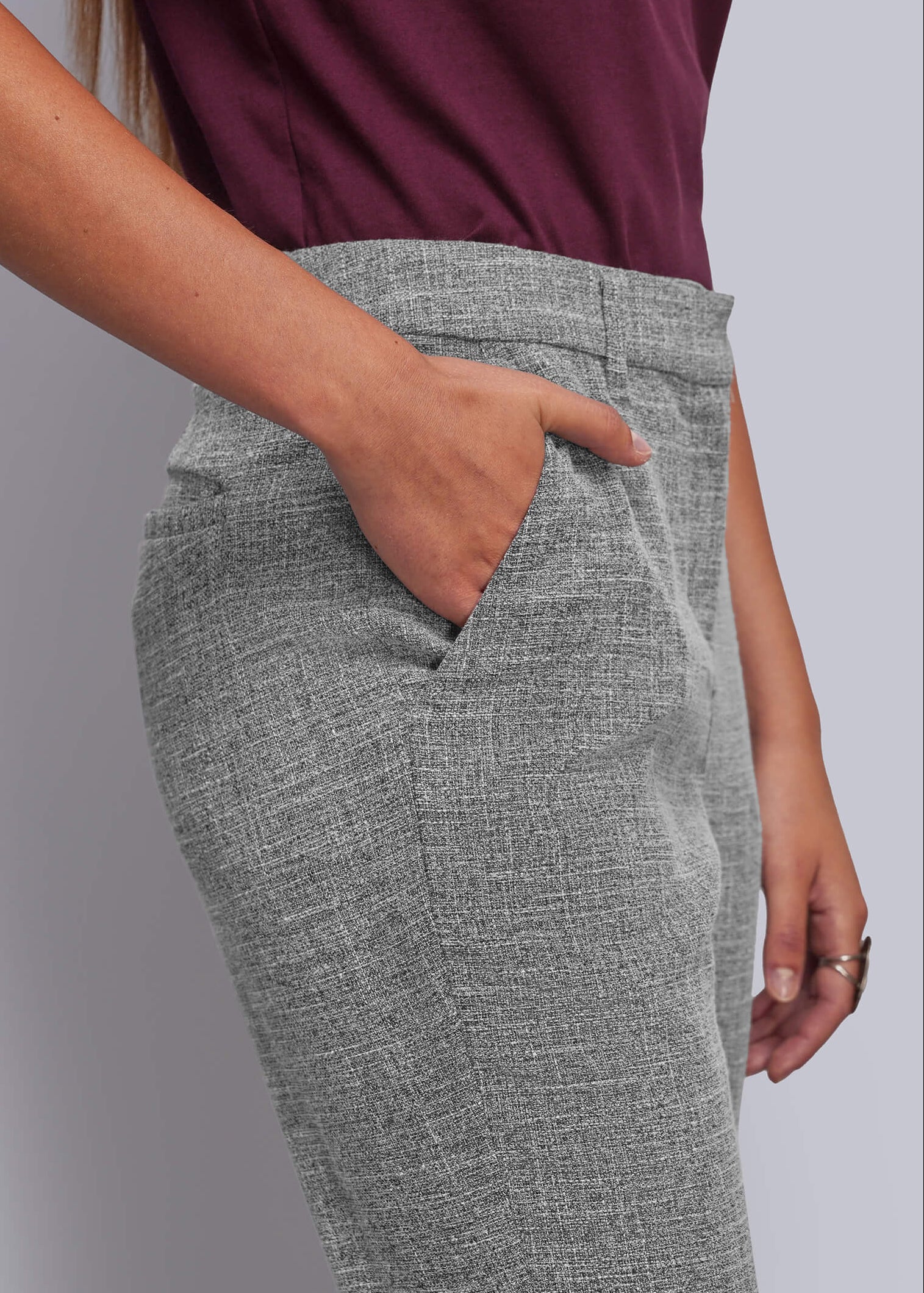 A close-up of a person wearing gray textured trousers with a side pocket, paired with a dark burgundy top, against a plain light gray background.