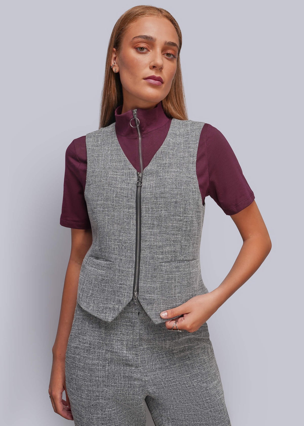 S=A woman modeling a gray zip-front vest over a short-sleeve burgundy top, paired with matching gray trousers, against a light gray studio background.