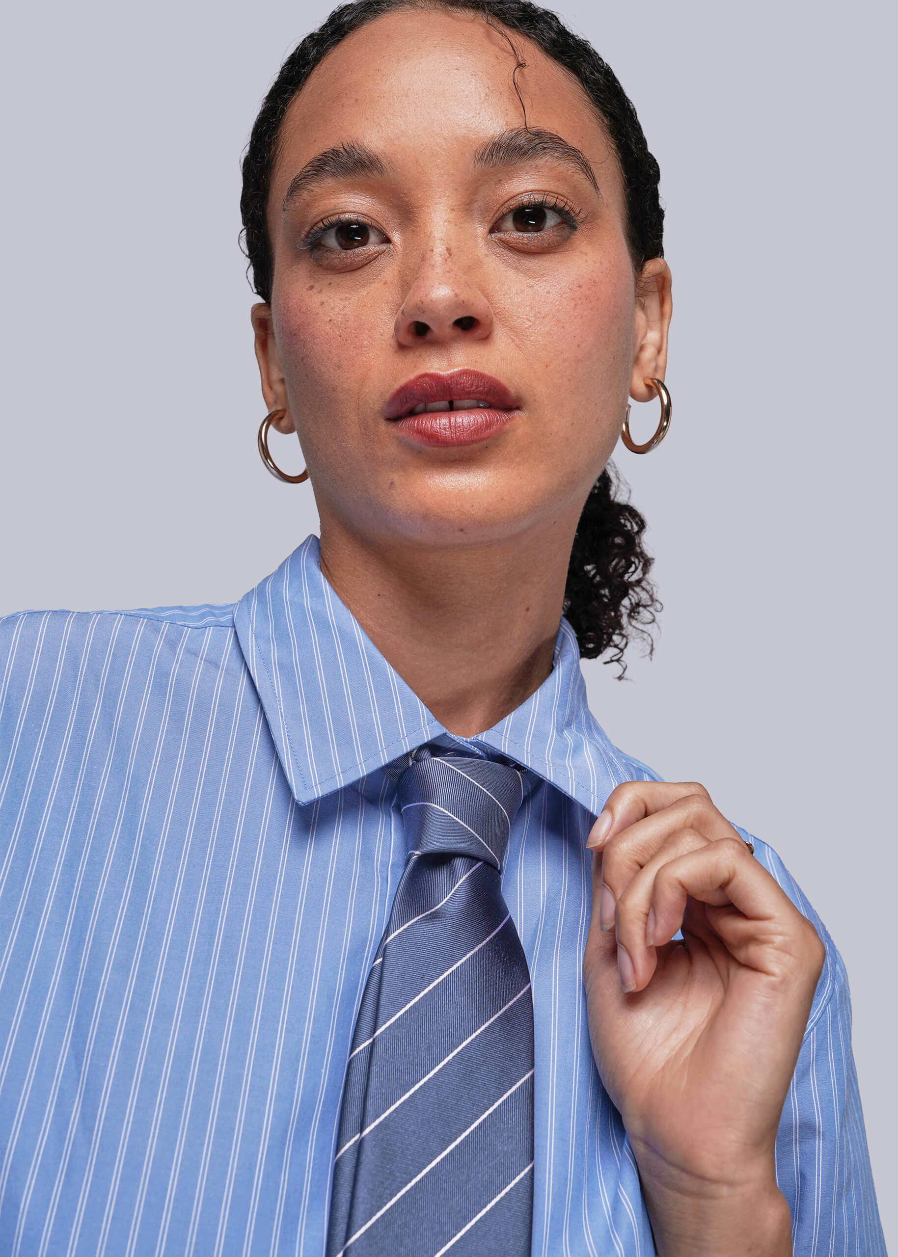 Person wearing a blue striped shirt and tie against a plain background