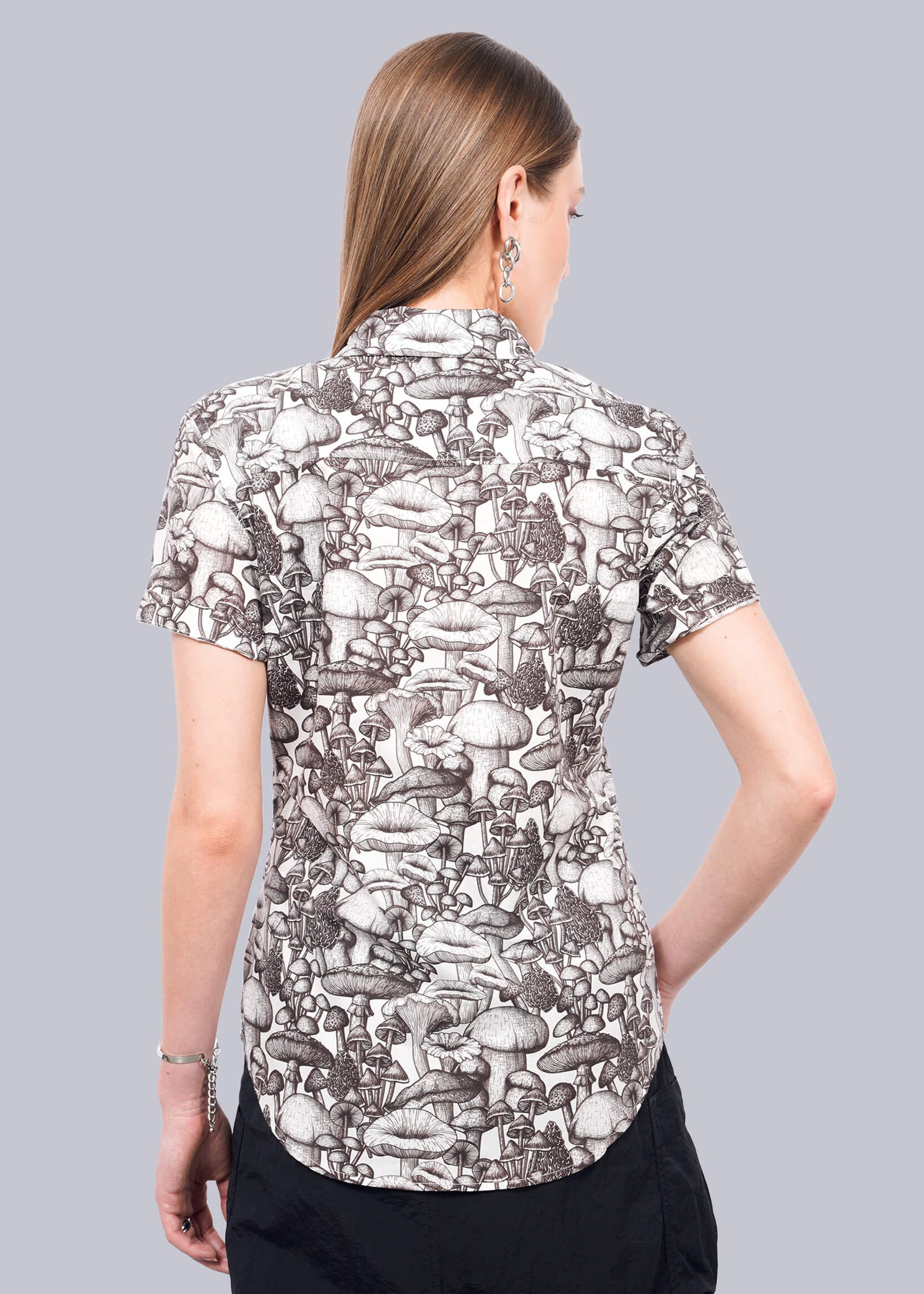 S= A person with straight, light brown hair wears The Essential Button Up—a short-sleeve, black and white mushroom-print shirt crafted from breathable cotton with Wildfang-branded buttons—paired with black pants. The background is plain white.