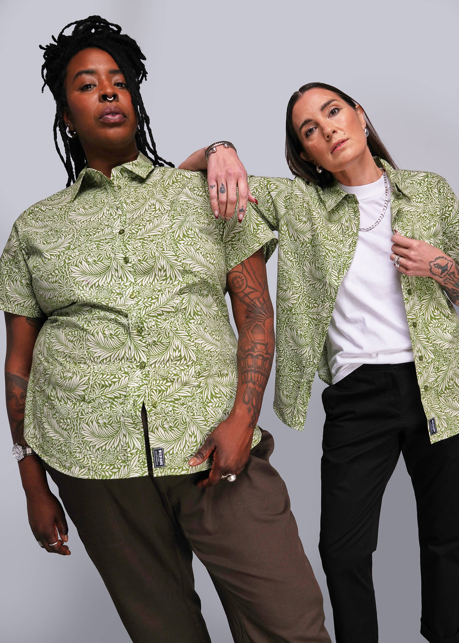 Two people wearing matching green patterned shirts against a gray background