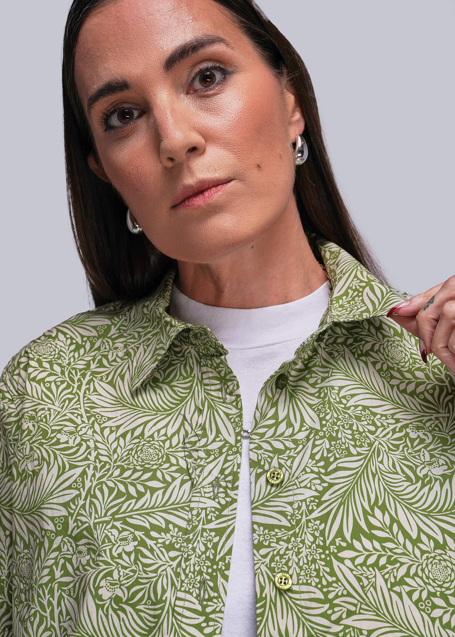 S=Woman wearing a green patterned shirt over a white top against a gray background