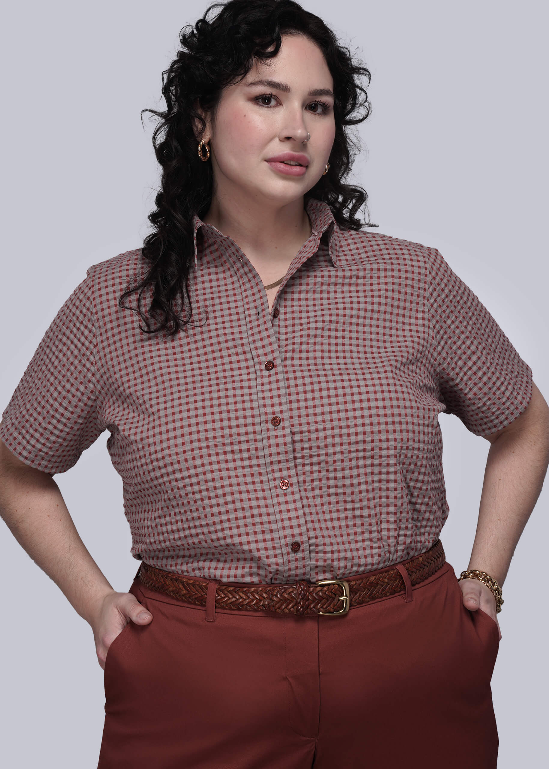 1X=Woman wearing a checkered shirt and red pants against a gray background