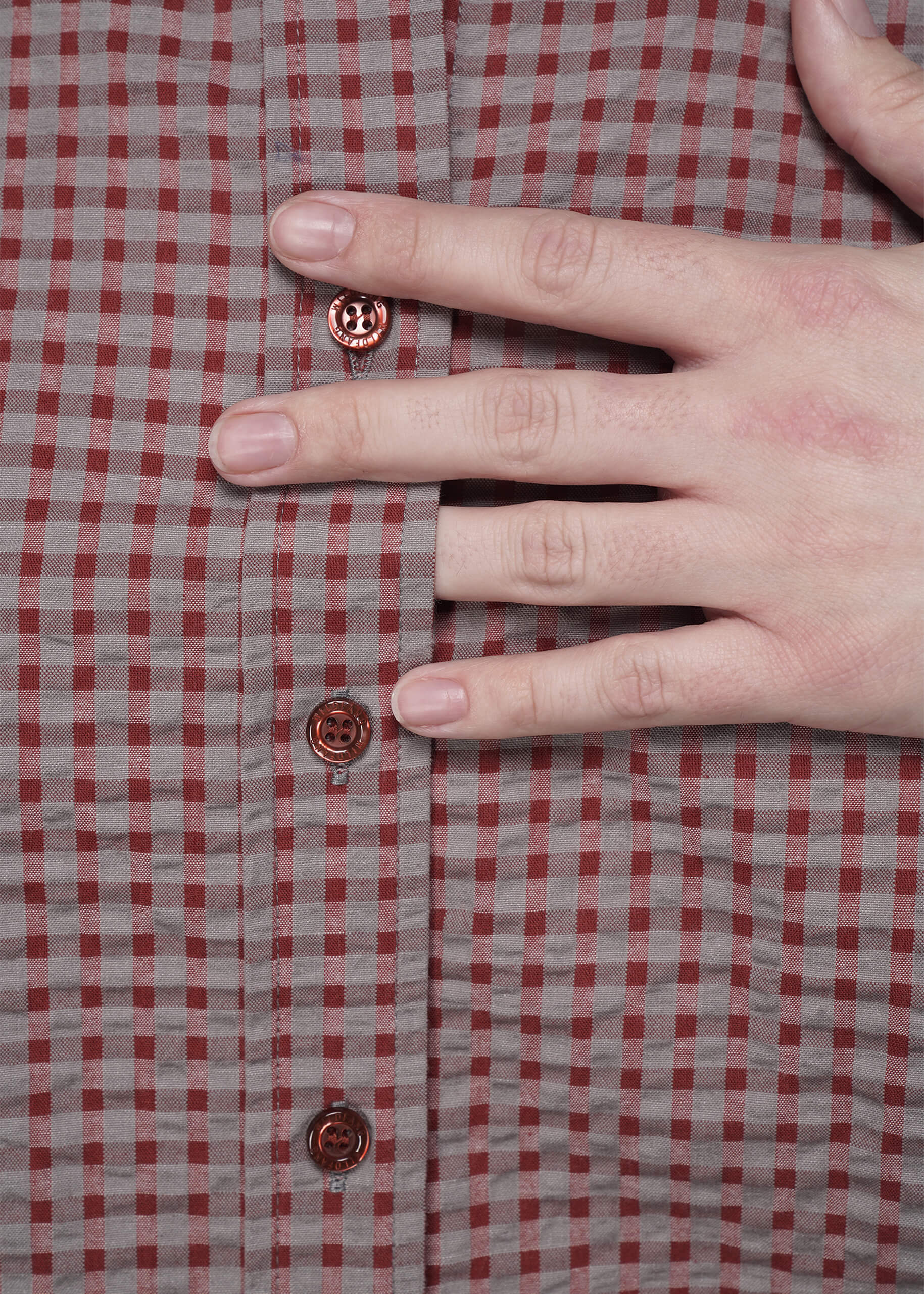 S=Hand pressing on a red and gray checkered shirt with visible buttons.