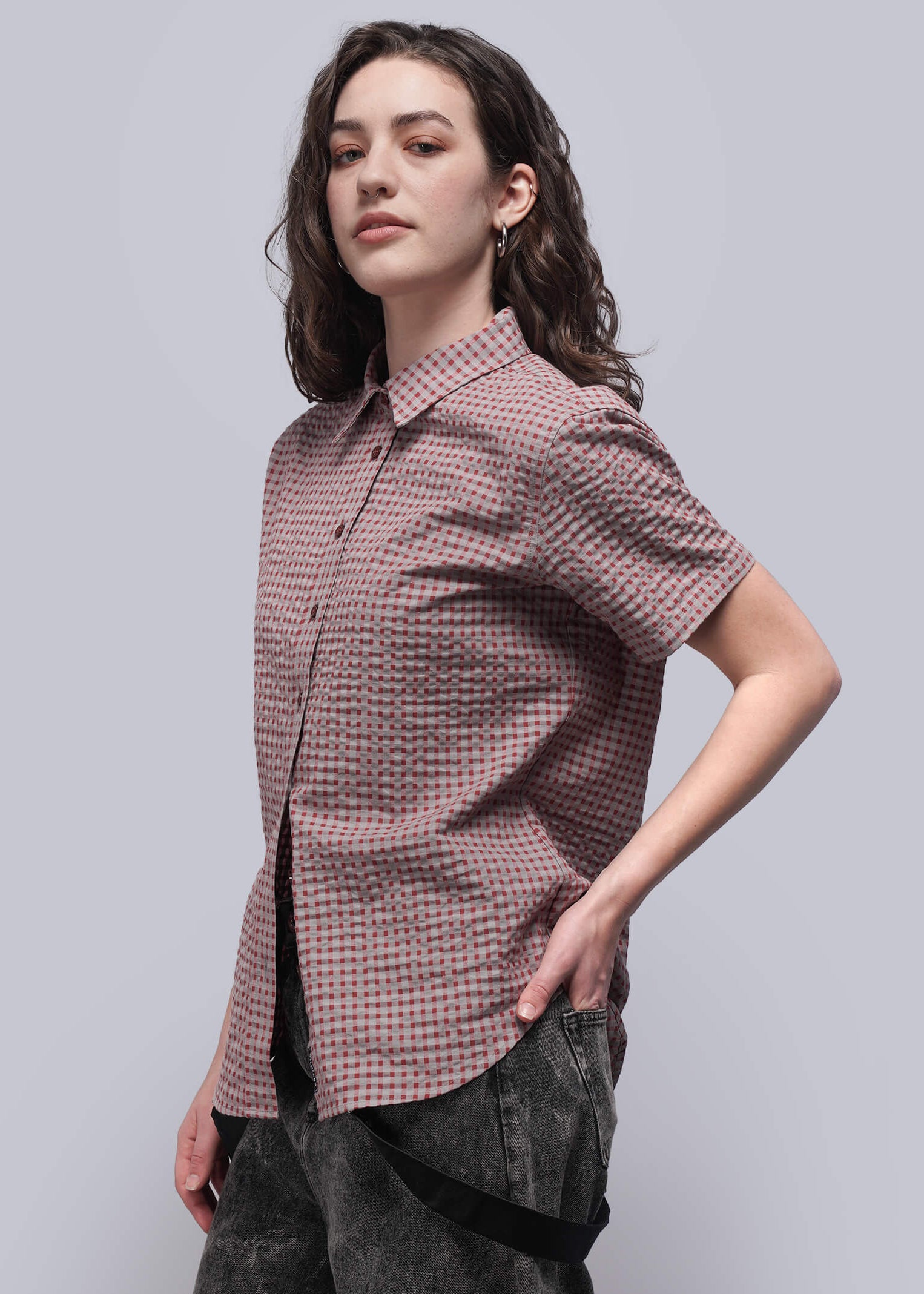 S=Woman wearing a patterned shirt and dark pants against a light gray background