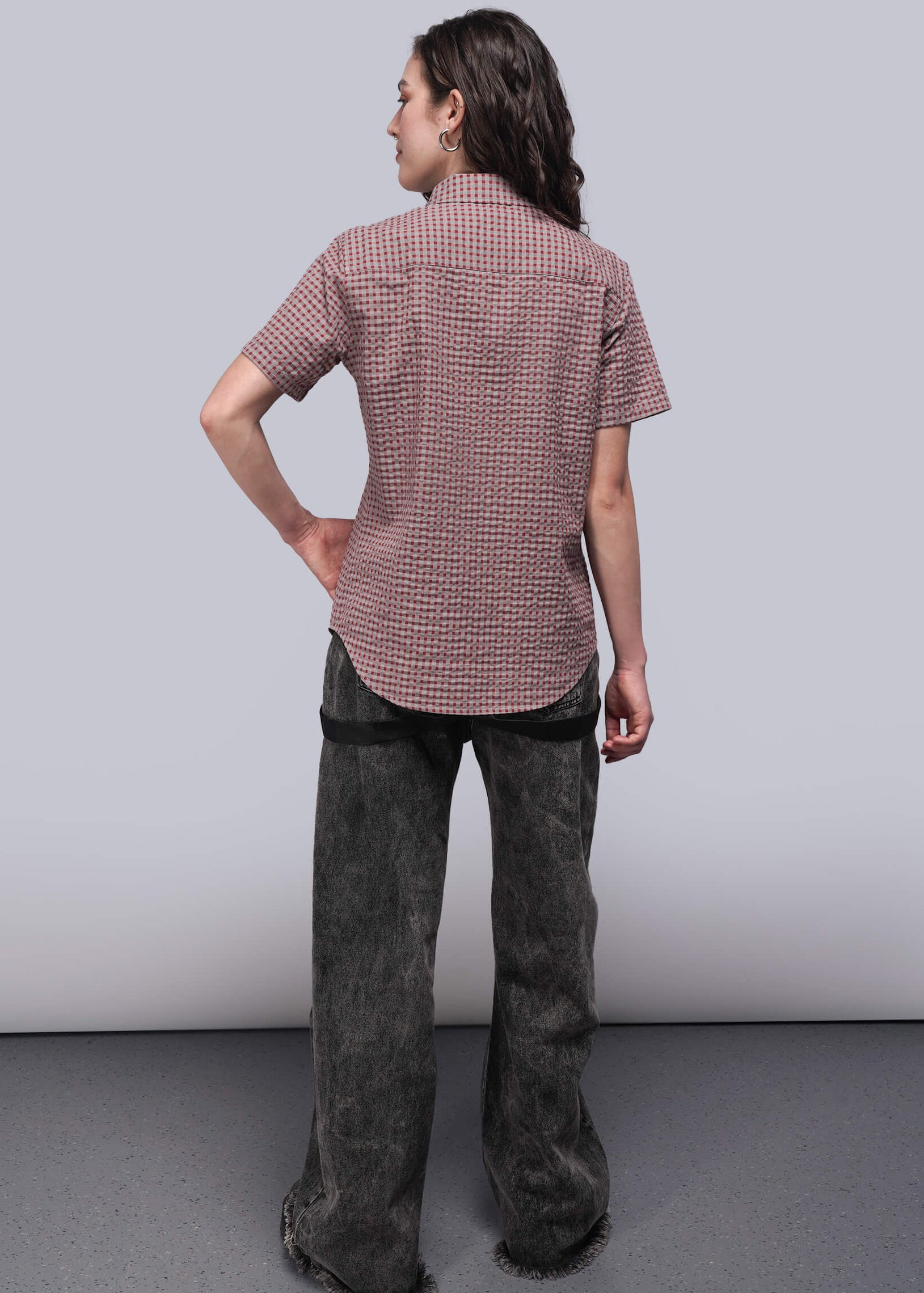 S=Person wearing a patterned shirt and dark pants against a plain background