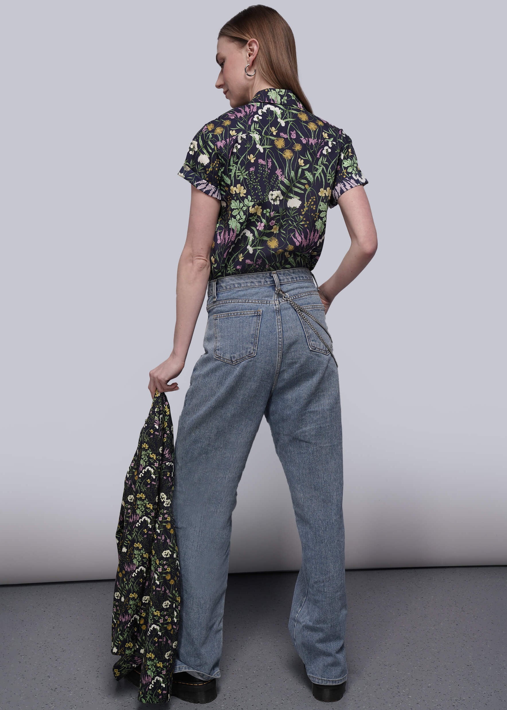 S=Back of person wearing a floral shirt and blue jeans holding a matching floral jacket against a plain background