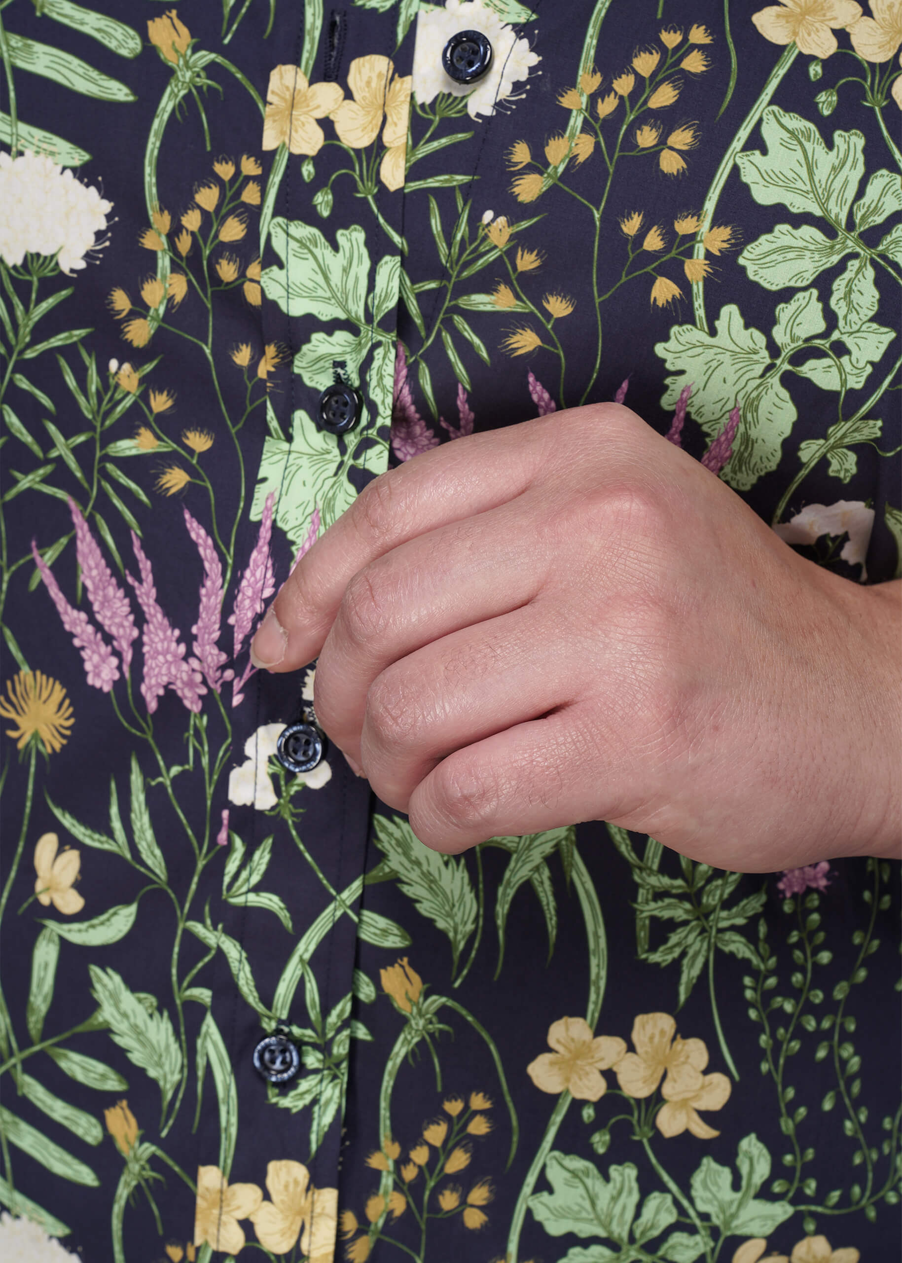 1X=Hand buttoning a floral-patterned shirt with a focus on the fabric design.