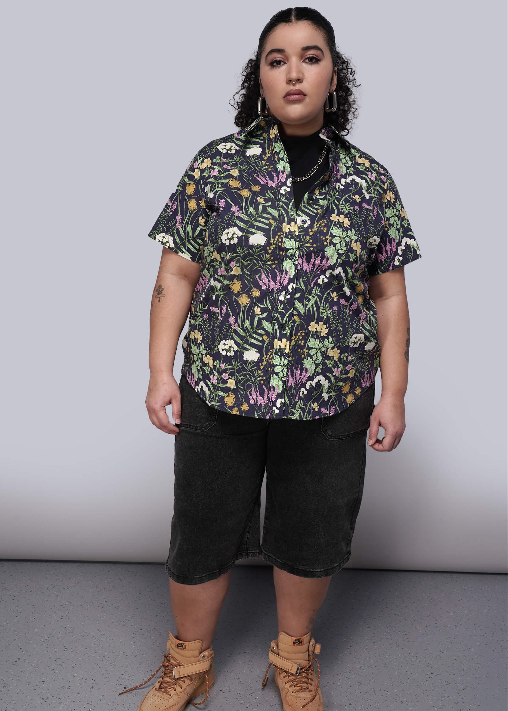 1X=Person wearing a floral shirt, black shorts, and brown boots on a plain background