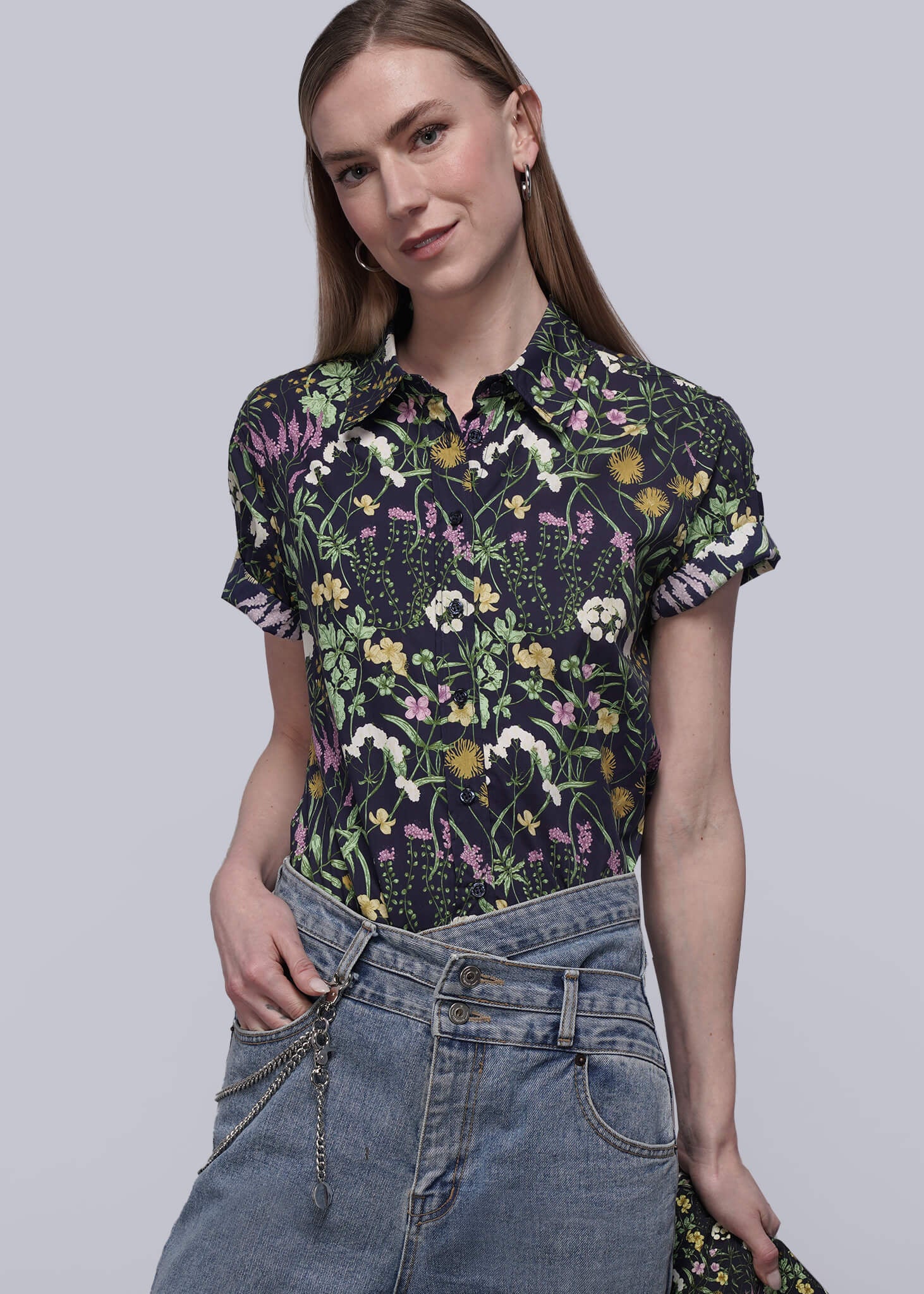 S=Woman wearing a floral shirt and jeans on a plain background