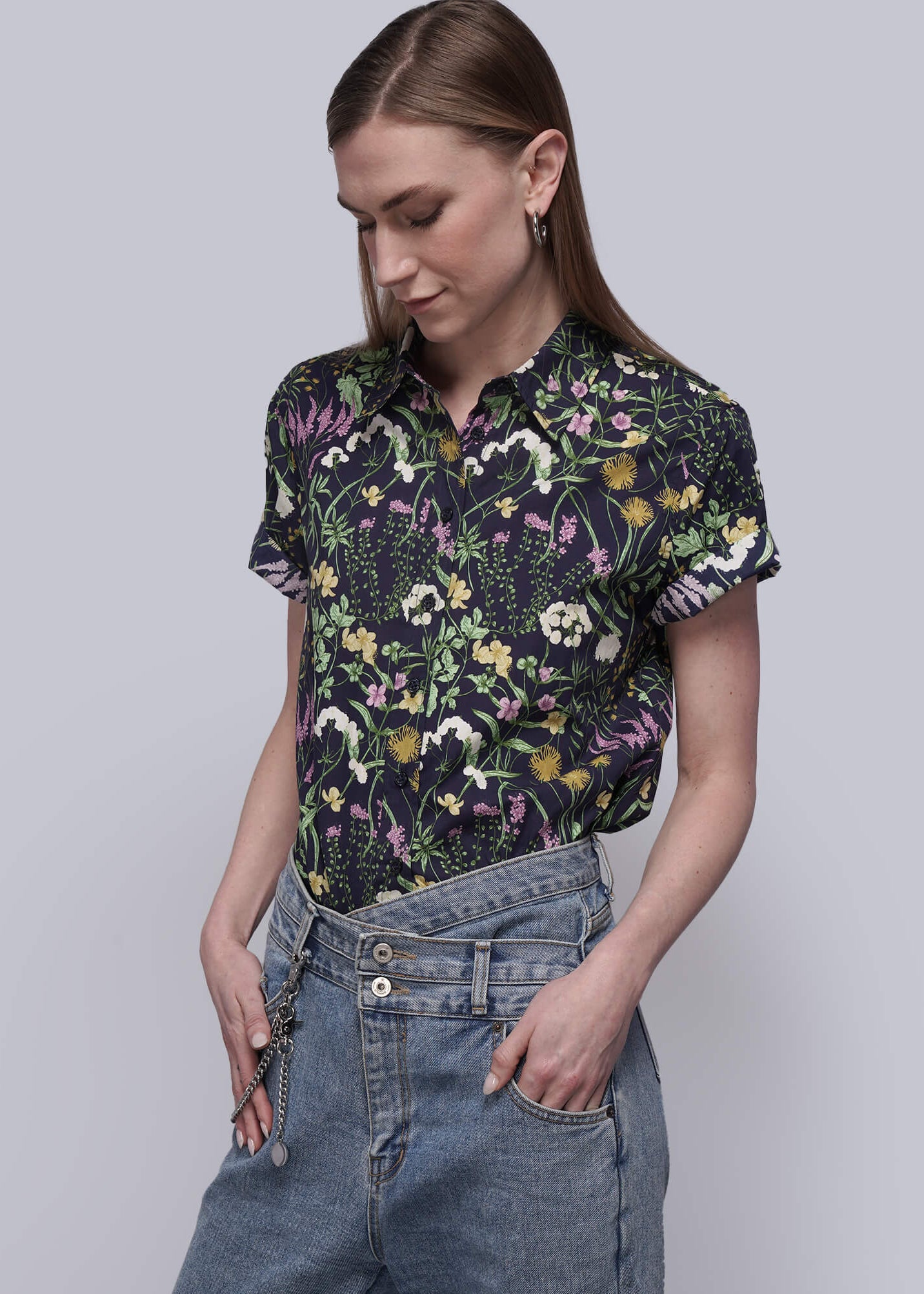 S=Woman wearing a floral patterned shirt and jeans against a plain background