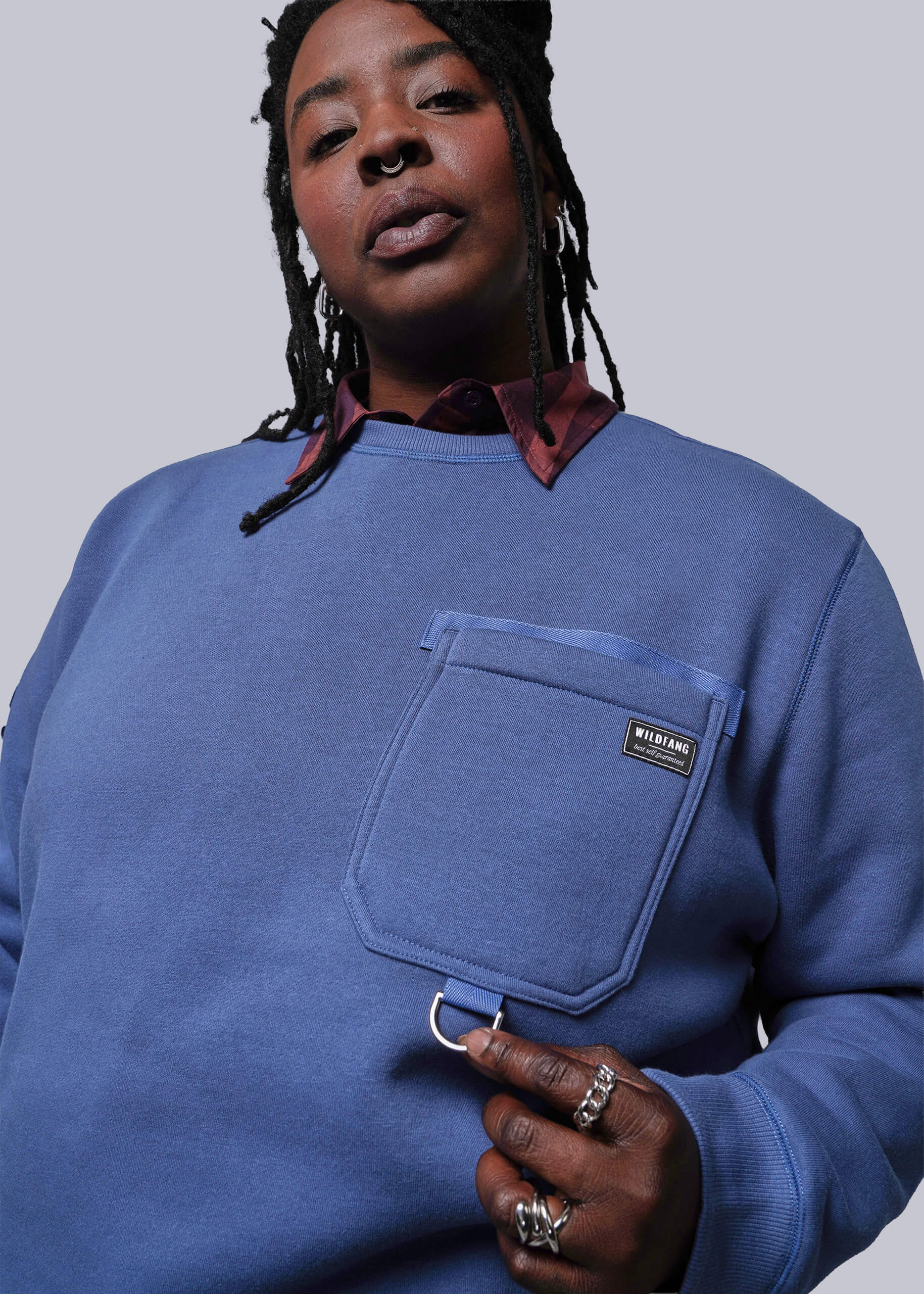 1X=Person wearing a blue sweatshirt with a pocket and visible brand logo on a plain background