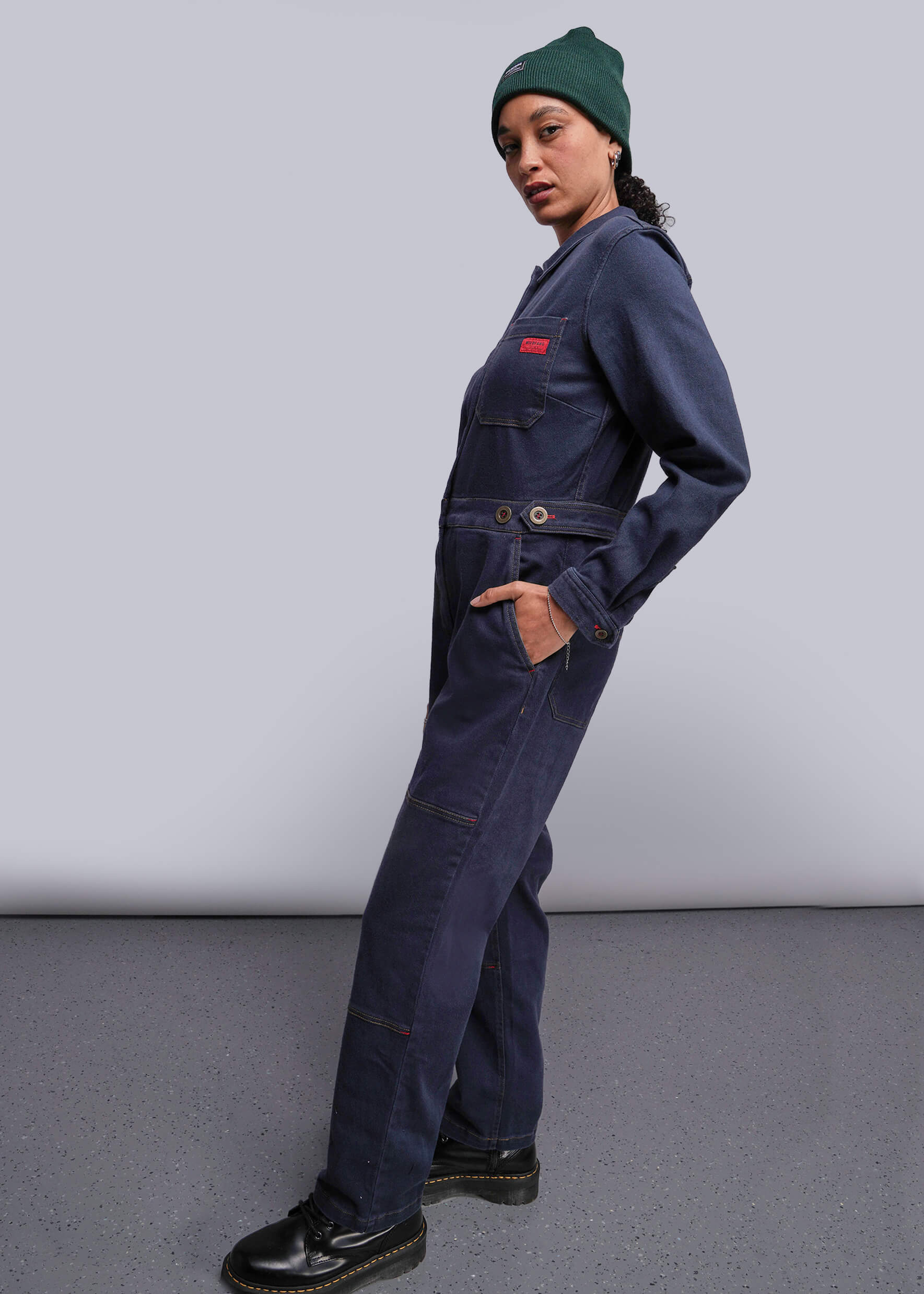 S=Person wearing a navy blue coverall with a green beanie on a plain background
