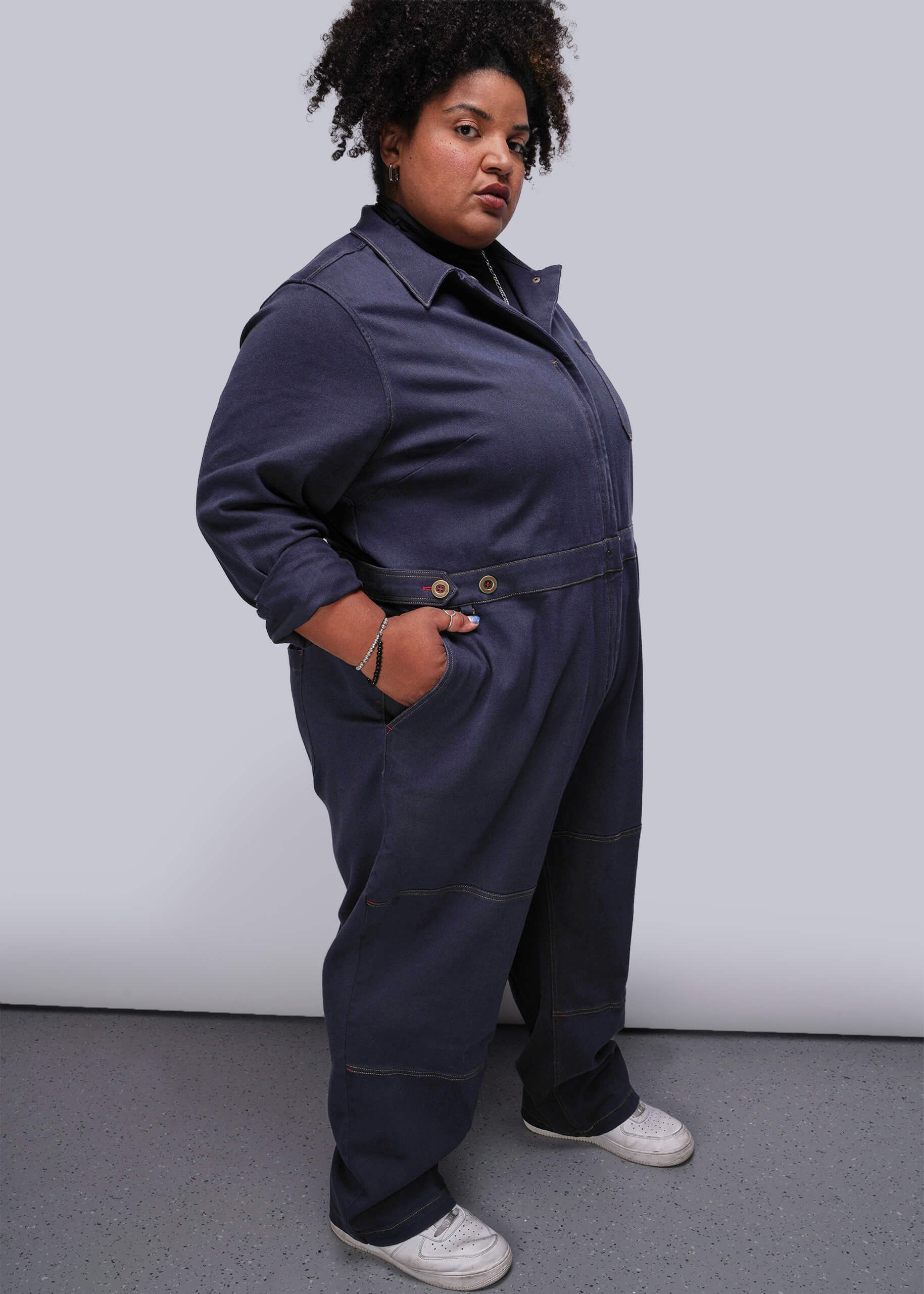 1X=Person wearing a navy blue jumpsuit against a plain background