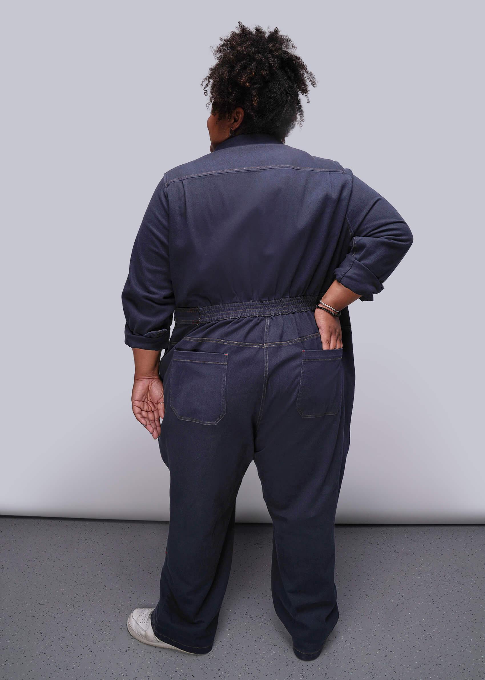 1X=Person wearing a navy blue jumpsuit against a plain background