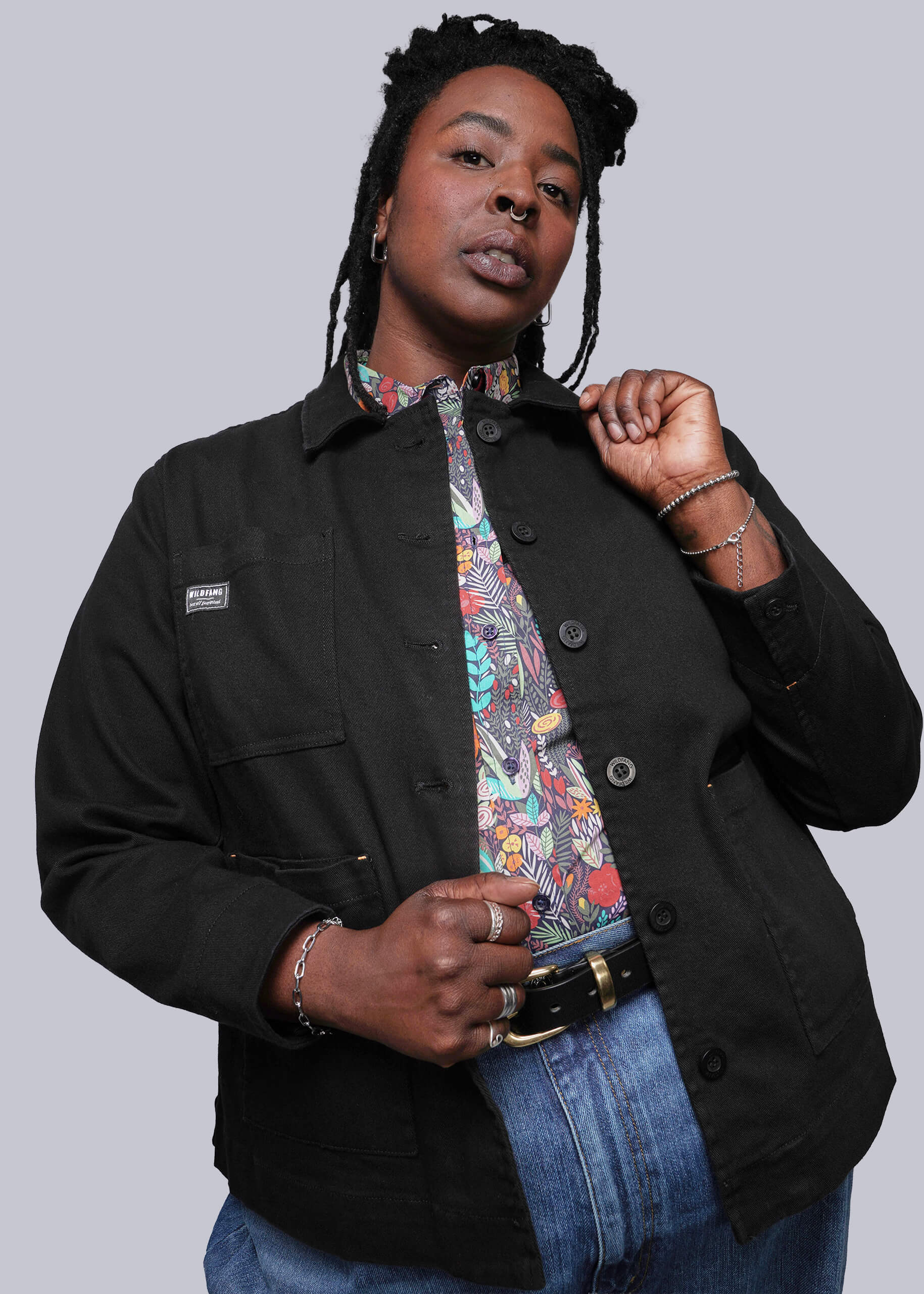 1X=Person wearing a black jacket over a colorful shirt with a plain background