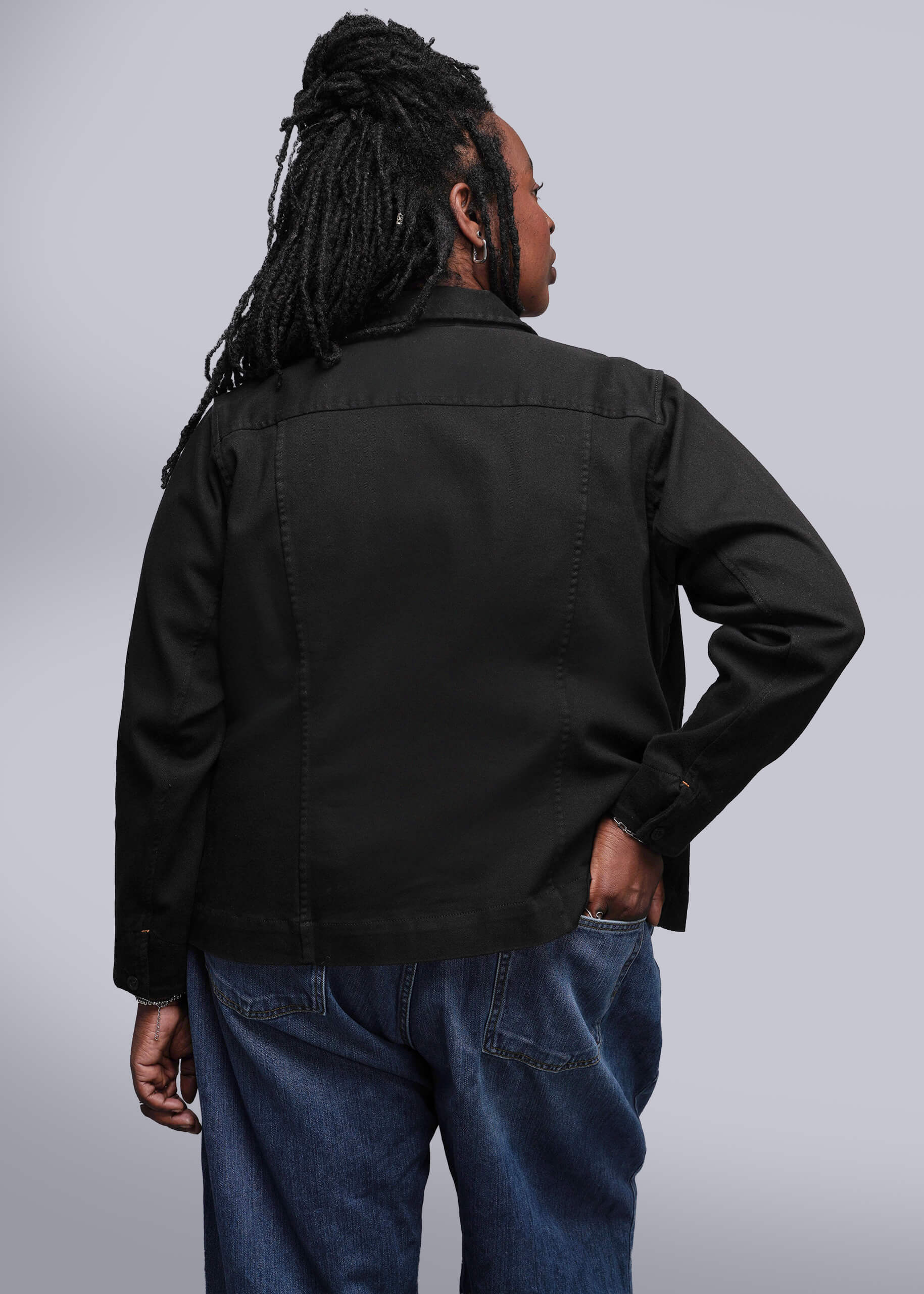 1X=Person wearing a black denim jacket and blue jeans against a plain background