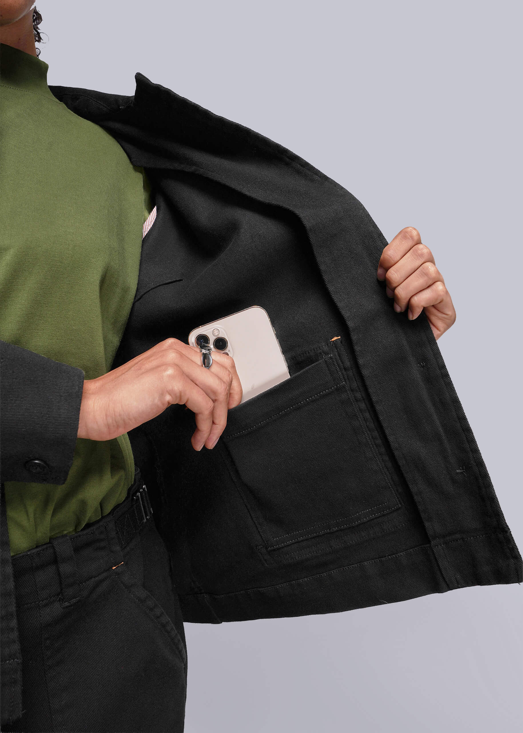 S=Person wearing a black jacket with a white phone in the pocket against a light gray background